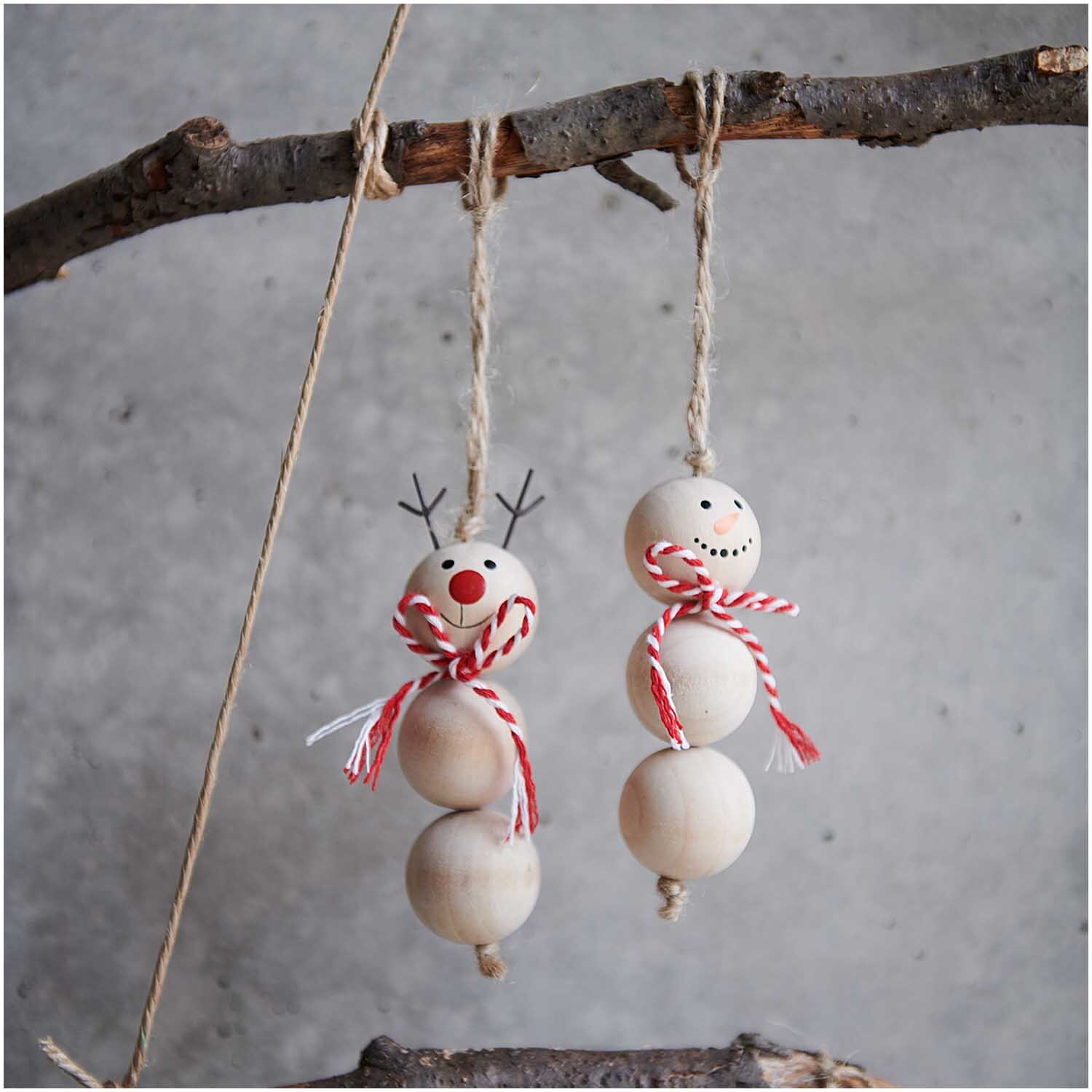 Hänger Schneemann Holzkugeln 3x9cm: Zwei Schneemann-Anhänger aus Holzkugeln mit roten Details, aufgehängt an einem Ast.
