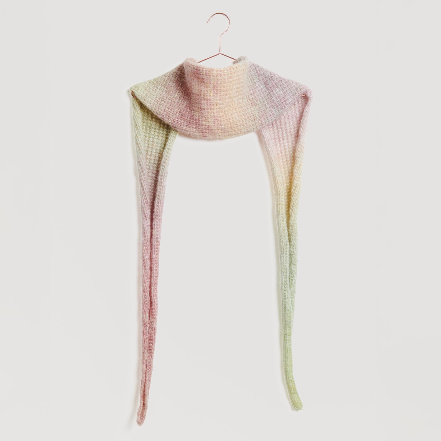 Creative Painted Power 100g 310m Farbe Earthy Pastels von Rico Design Ein langer, gestrickter Schal in sanften Pastelltönen hängt an einem Haken. Der Schal zeigt einen Farbverlauf von Rosa zu Grün. Marke: Modell Legeware. Ideal für stilvolle Wintermode.