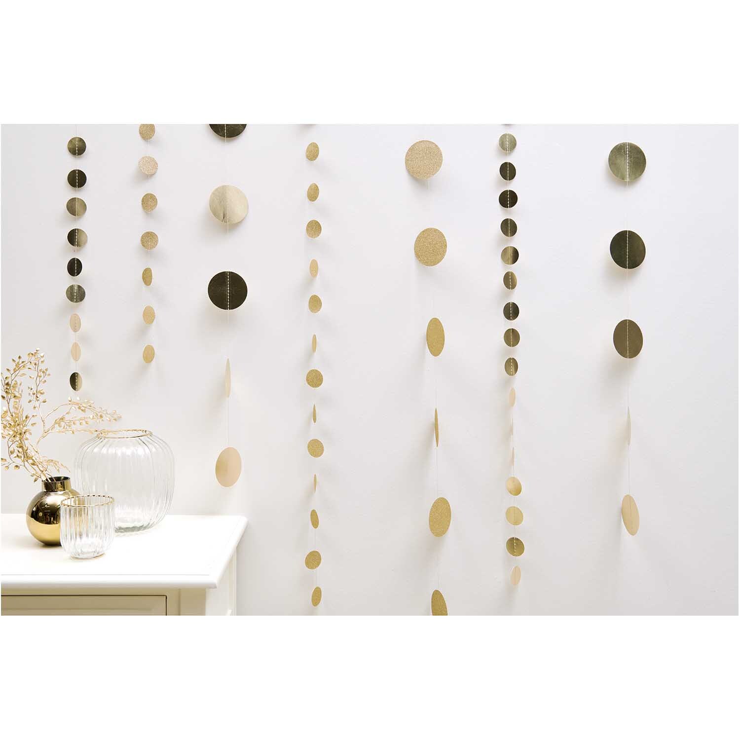 Genähte Girlande Kreise 3,8cm Glitter-gold 2m von Rico Design Genähte Girlande Kreise in Glitter-gold von Rico Design, dekorativ an einer weißen Wand hängend. Ideal für festliche Anlässe.