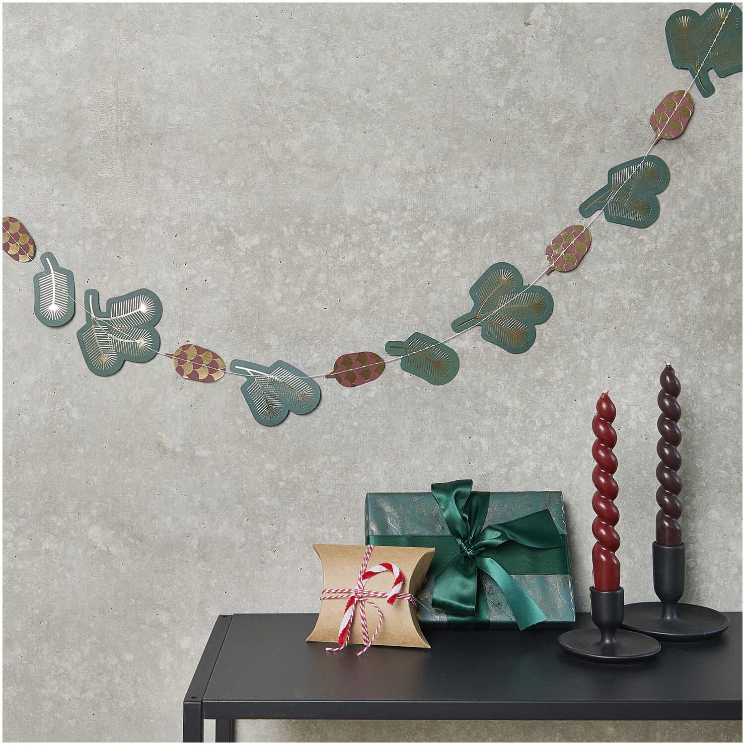 Paper Poetry genähte Girlande Zweige 2,3m von Rico Design Paper Poetry genähte Girlande Zweige 2,3m von Rico Design schmückt eine Wand über einem Tisch mit Geschenken und Kerzen.