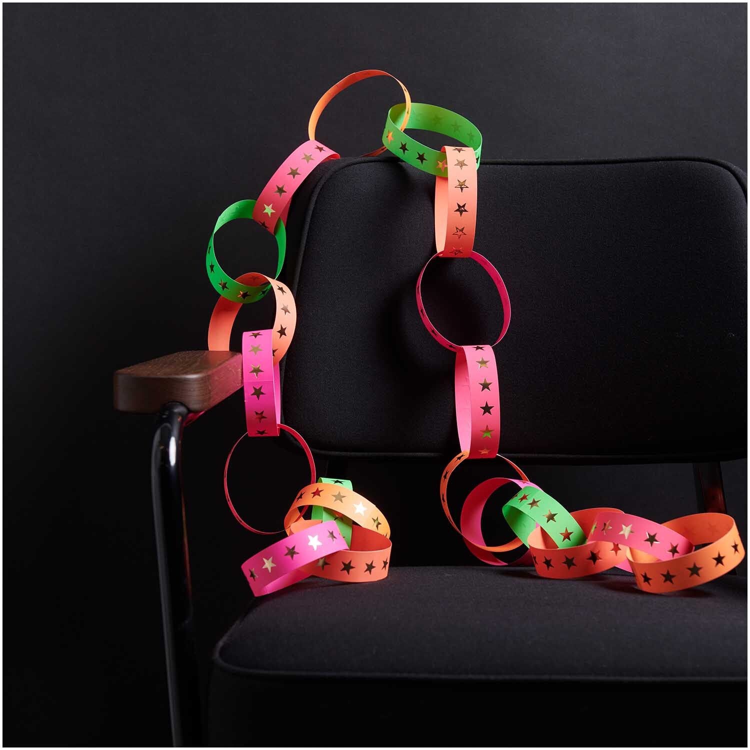 Paper Poetry Fröbelstreifen neon Sterne L 40 Stück von Rico Design Paper Poetry Fröbelstreifen neon Sterne L 40 Stück: Bunte Papierstreifen mit Sternenmuster, dekorativ auf einem schwarzen Stuhl arrangiert.