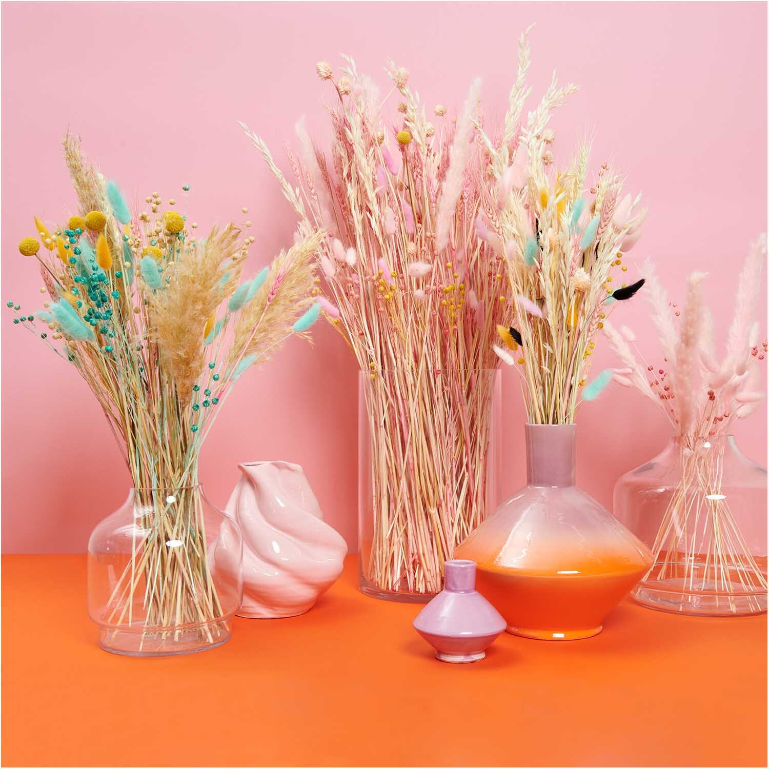 Getrockneter Flachs türkis 60-75cm 100g von Rico Design Getrockneter Flachs türkis 60-75cm 100g in eleganten Vasen, umgeben von pastellfarbenen Trockenblumen, auf einem orangefarbenen Tisch.
