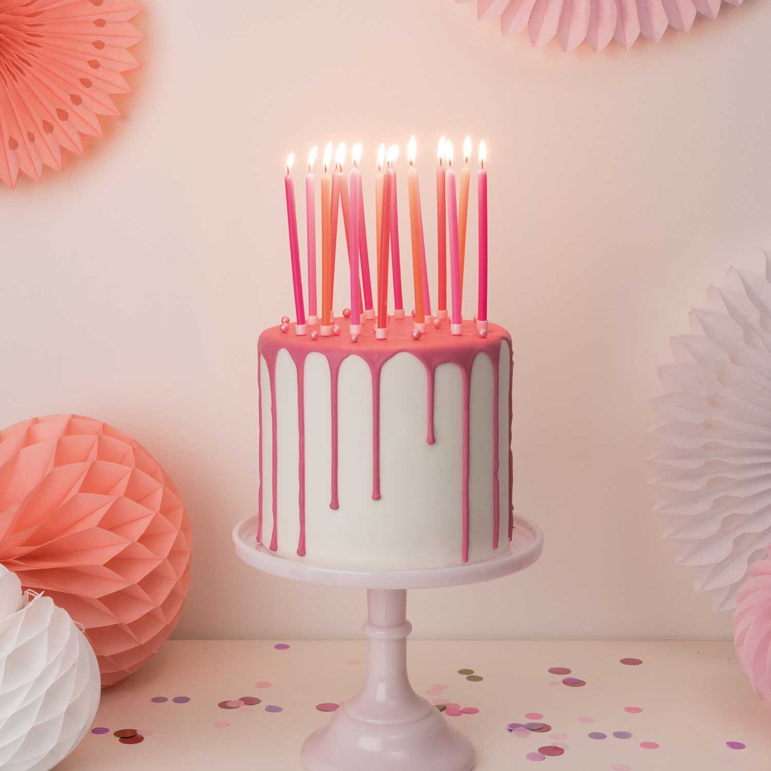 Kerzen lang 16 Stück auf einer Torte mit rosa Tropfglasur, umgeben von rosa Dekorationen. Marke: Rico Design.