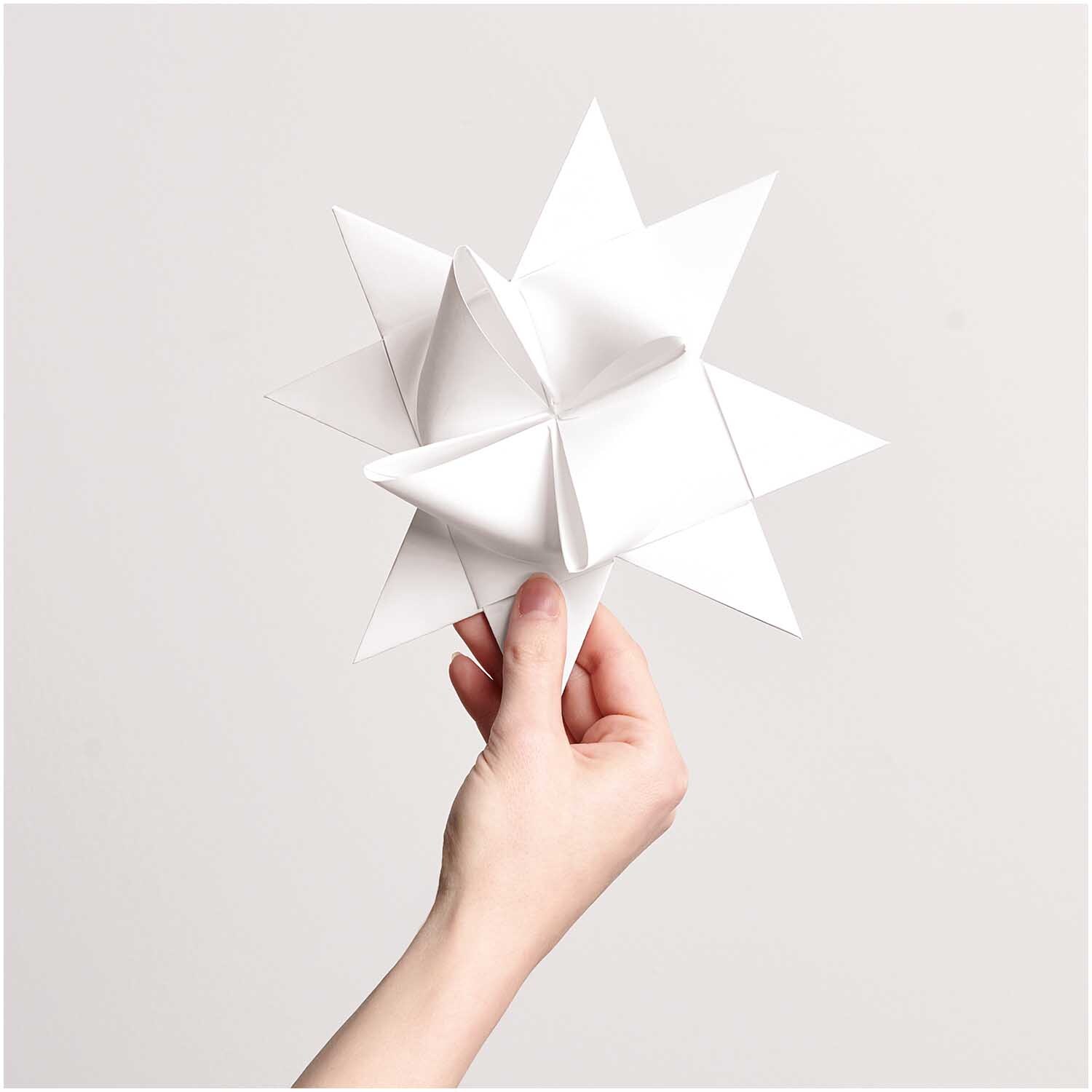 Paper Poetry Fröbelstreifen XXL 180g/m2 20 pièces Couleur Blanc from Rico Design Paper Poetry Fröbelstreifen XXL in Weiß, gefaltet zu einem dekorativen Stern, gehalten von einer Hand. Ideal für kreative Bastelprojekte.