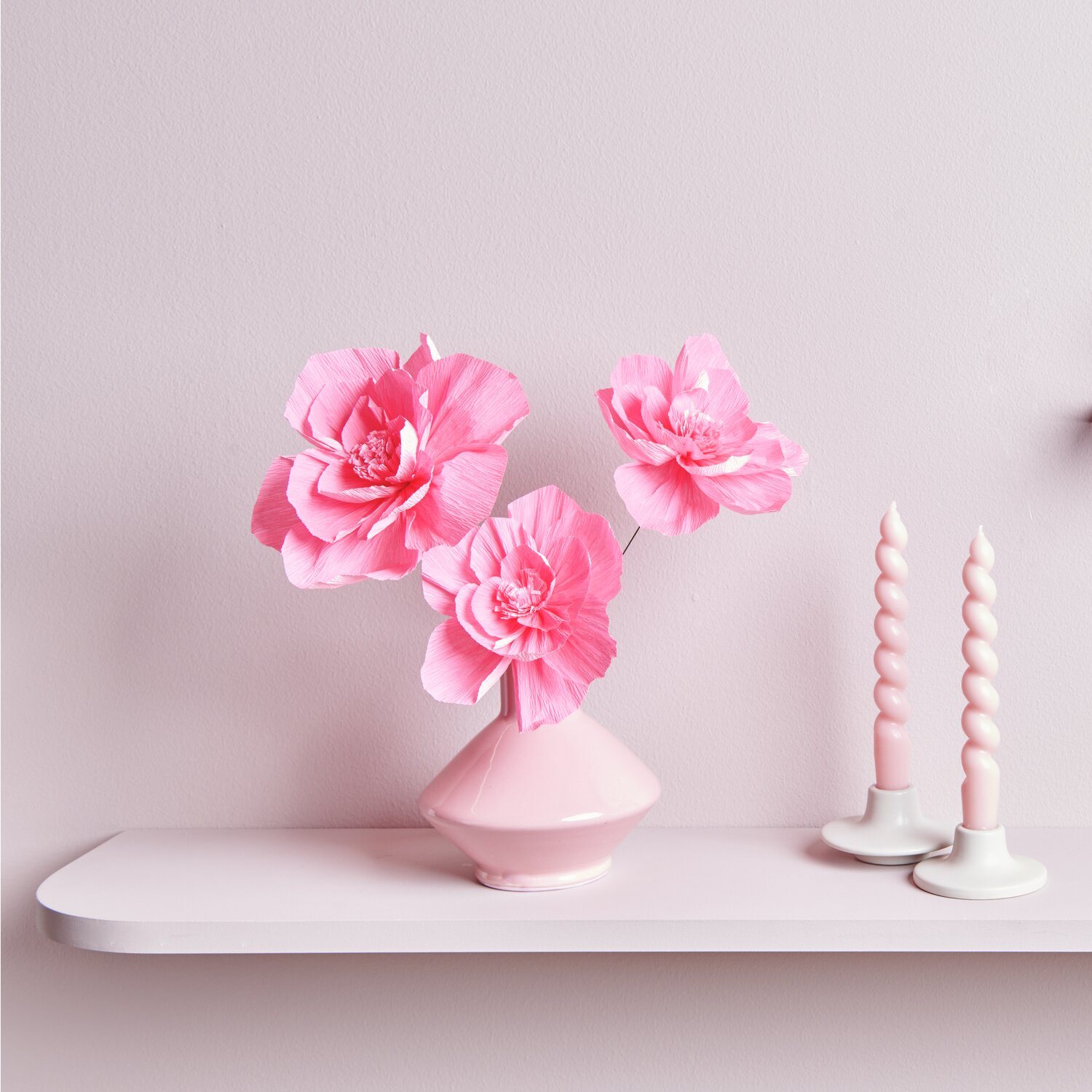 Krepppapier Blüten in Neonpink von Rico Design in Vase auf Regal mit zwei Kerzen.