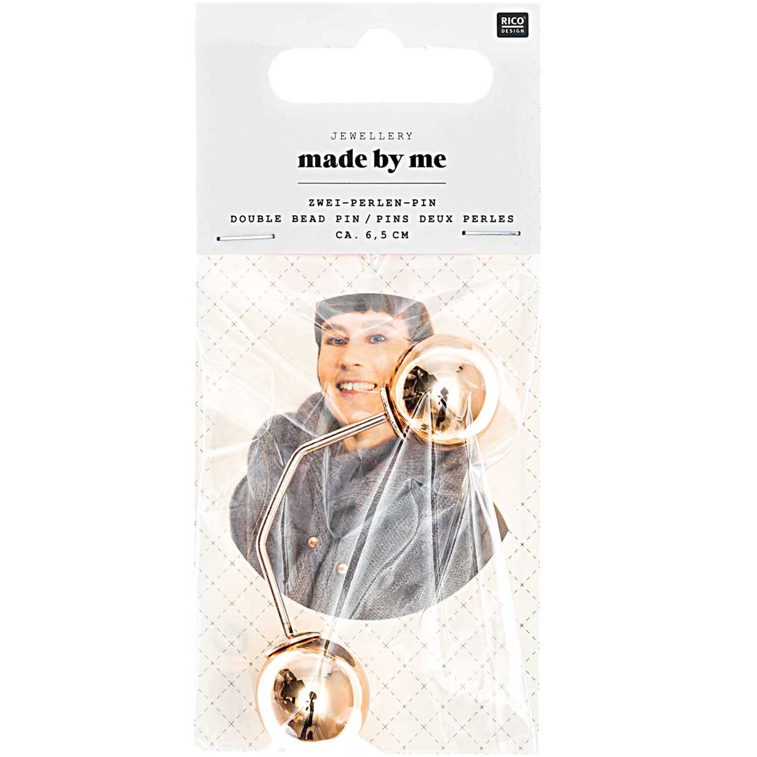 Zwei-Perlen-Pin 65mm 1 Stück Farbe Roségold von Rico Design Zwei-Perlen-Pin in Roségold von Rico Design, 65mm lang, auf einer Verpackung mit lächelnder Person.