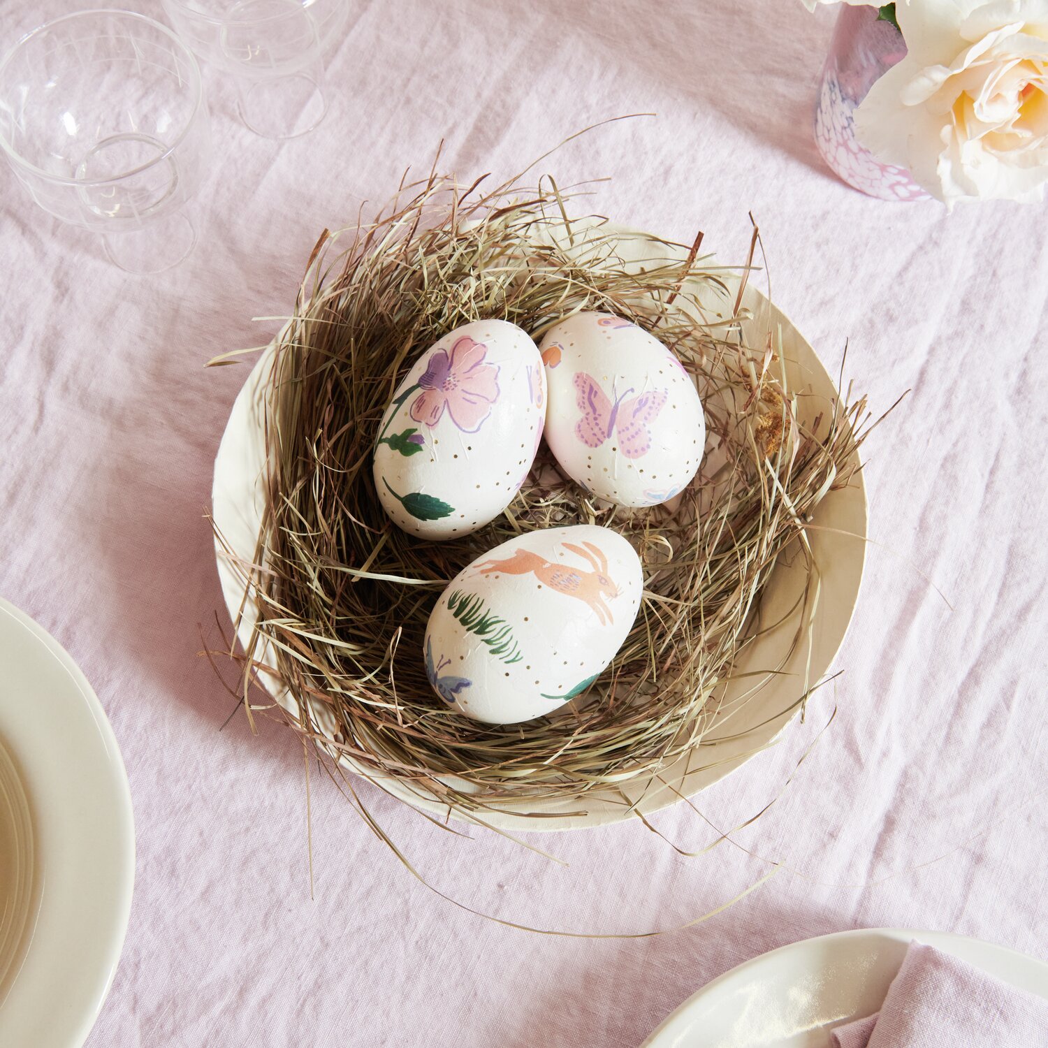 Paper Patch Papier Frühlingswiese: Drei dekorierte Eier mit Blumenmotiven in einem Nest auf einem Tisch.