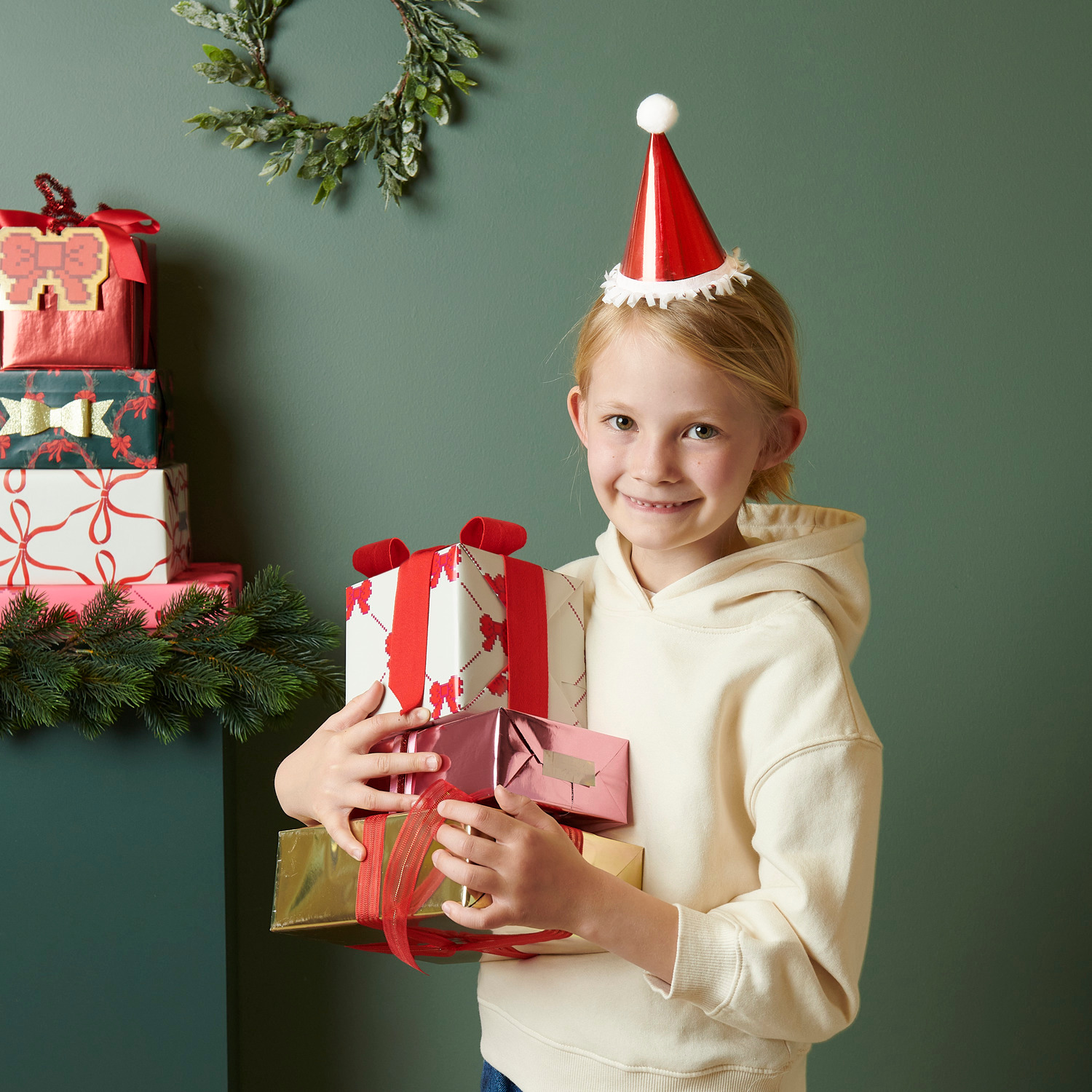 Mini-Partyhüte Weihnachtsmann Ø8x14cm 8 Stück von Rico Design Mini-Partyhüte Weihnachtsmann: Kind mit roten Hüten von Rico Design, hält Geschenke vor grünem Hintergrund. Ø8x14cm 8 Stück.