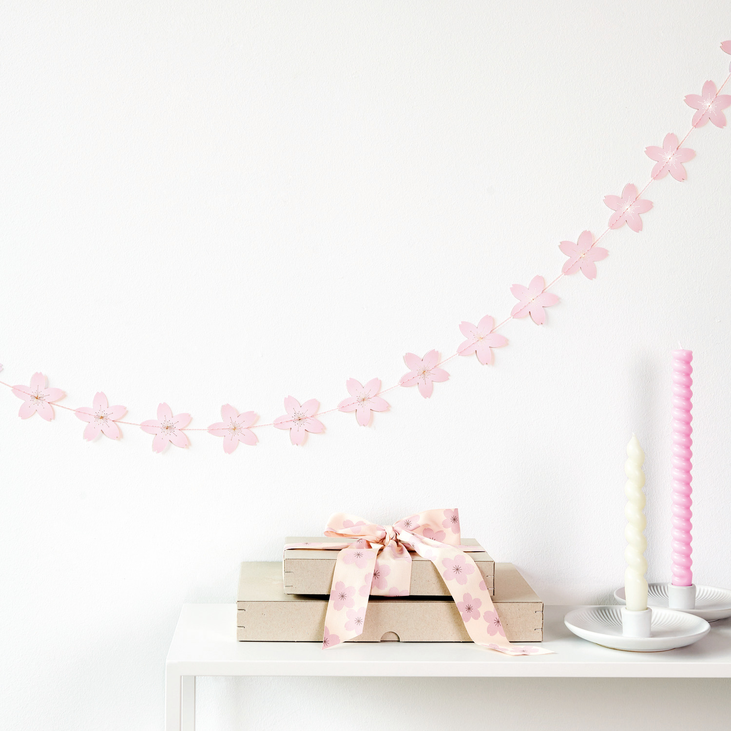 Genähte Girlande Kirschblüten von Rico Design: Rosa Blüten-Girlande dekoriert einen Tisch mit Kerzen und Geschenkboxen.
