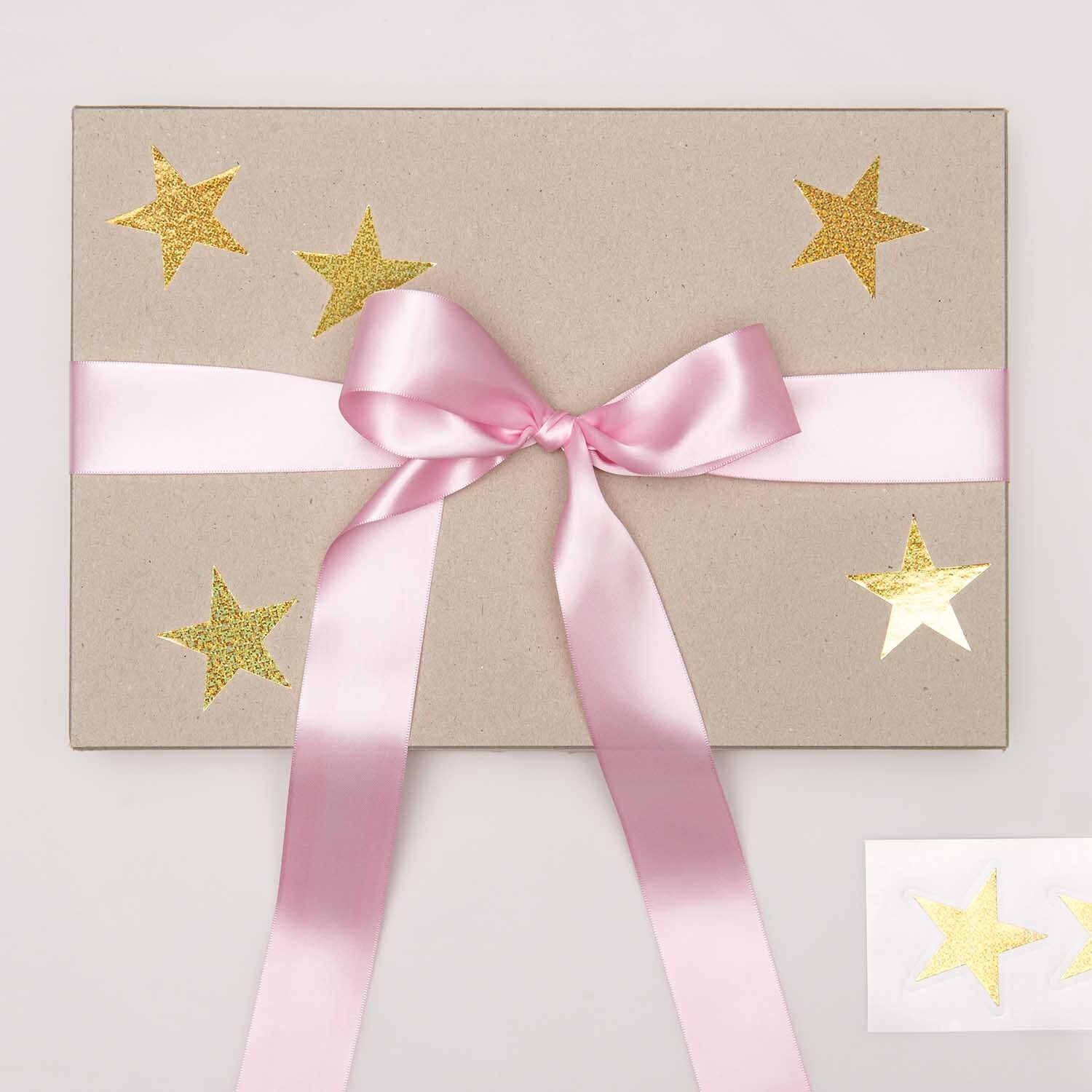 Paper Poetry Sticker Sterne 5cm 120 Stück auf der Rolle Hot Foil Farbe Gold-Holographisch von Rico Design Paper Poetry Sticker Sterne auf Geschenkbox mit rosa Schleife, gold-holographisch glänzend.