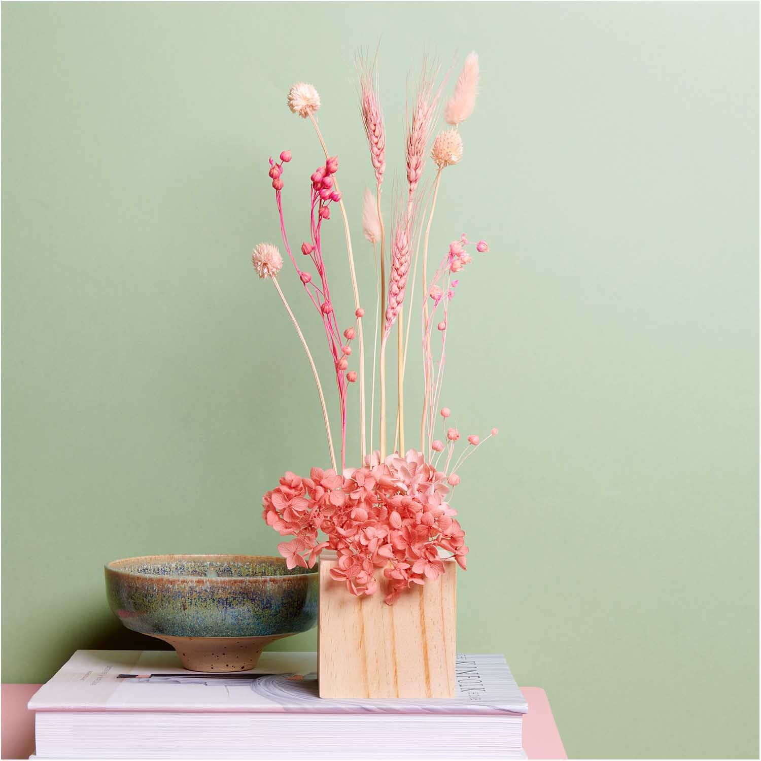 Trockenblumenstrauß pastell-pink 30cm in Vase, 13-teilig, auf Bücherstapel vor grünem Hintergrund.