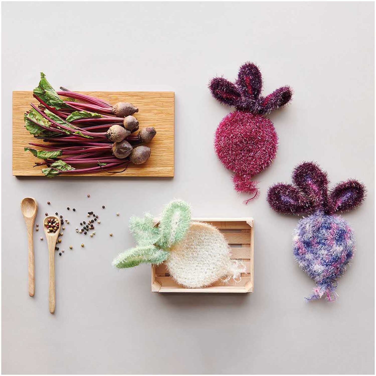 Creative Bubble: Handgestrickte Gemüseformen aus Rico Design Garn in Creme, dekoriert mit Holzlöffeln und Pfefferkörnern.