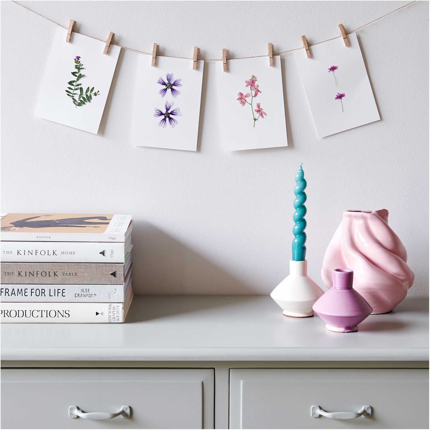 Gepresste Blüten Stockrose violett 8 Stück von Rico Design Gepresste Blüten Stockrose violett von Rico Design, dekorativ auf Karten an einer Leine präsentiert, vor einem stilvollen Regal mit Vasen und Büchern.