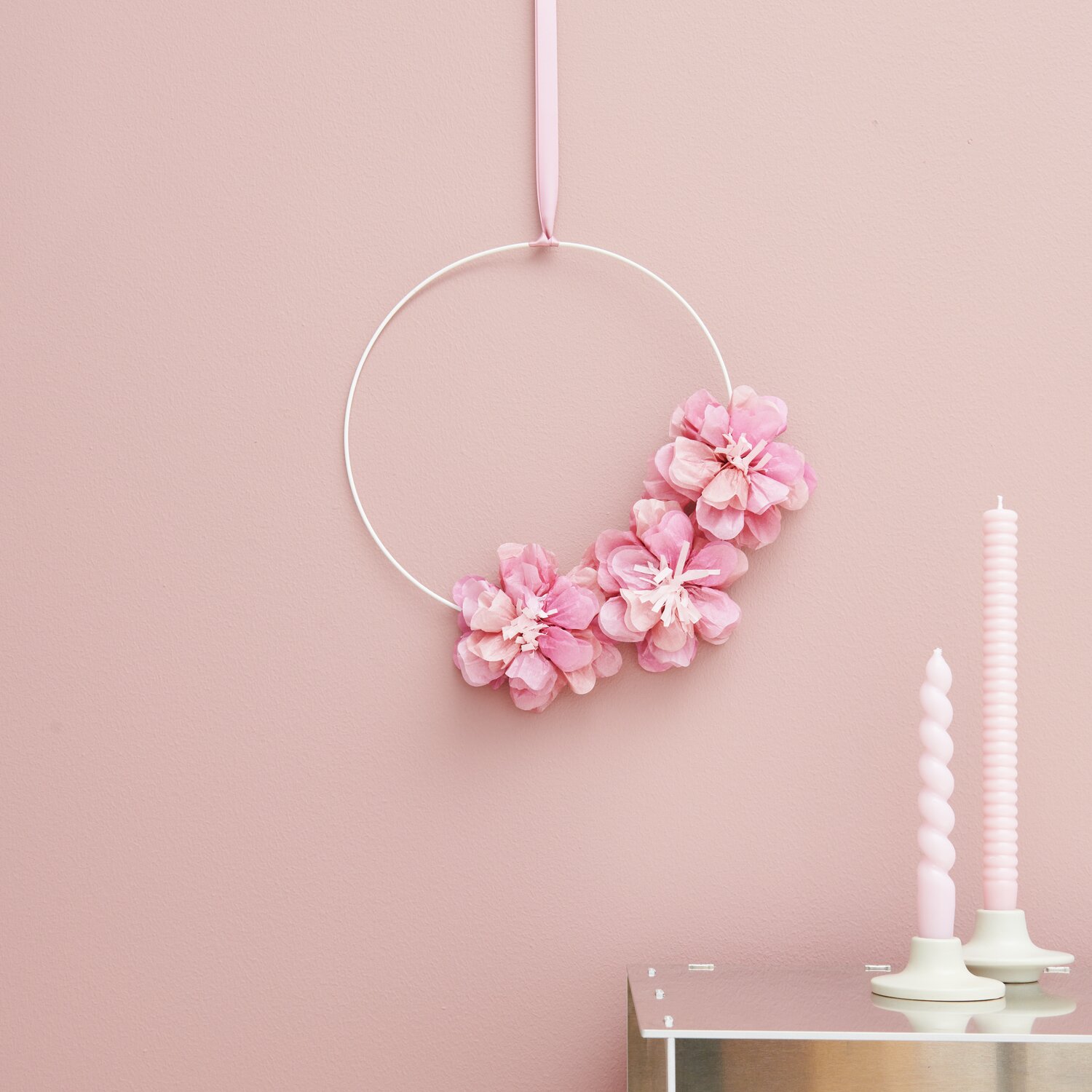 Seidenpapierblumen Wildrose Rosa von Rico Design: Drei zarte Blumen an einem weißen Ring vor rosa Wand.