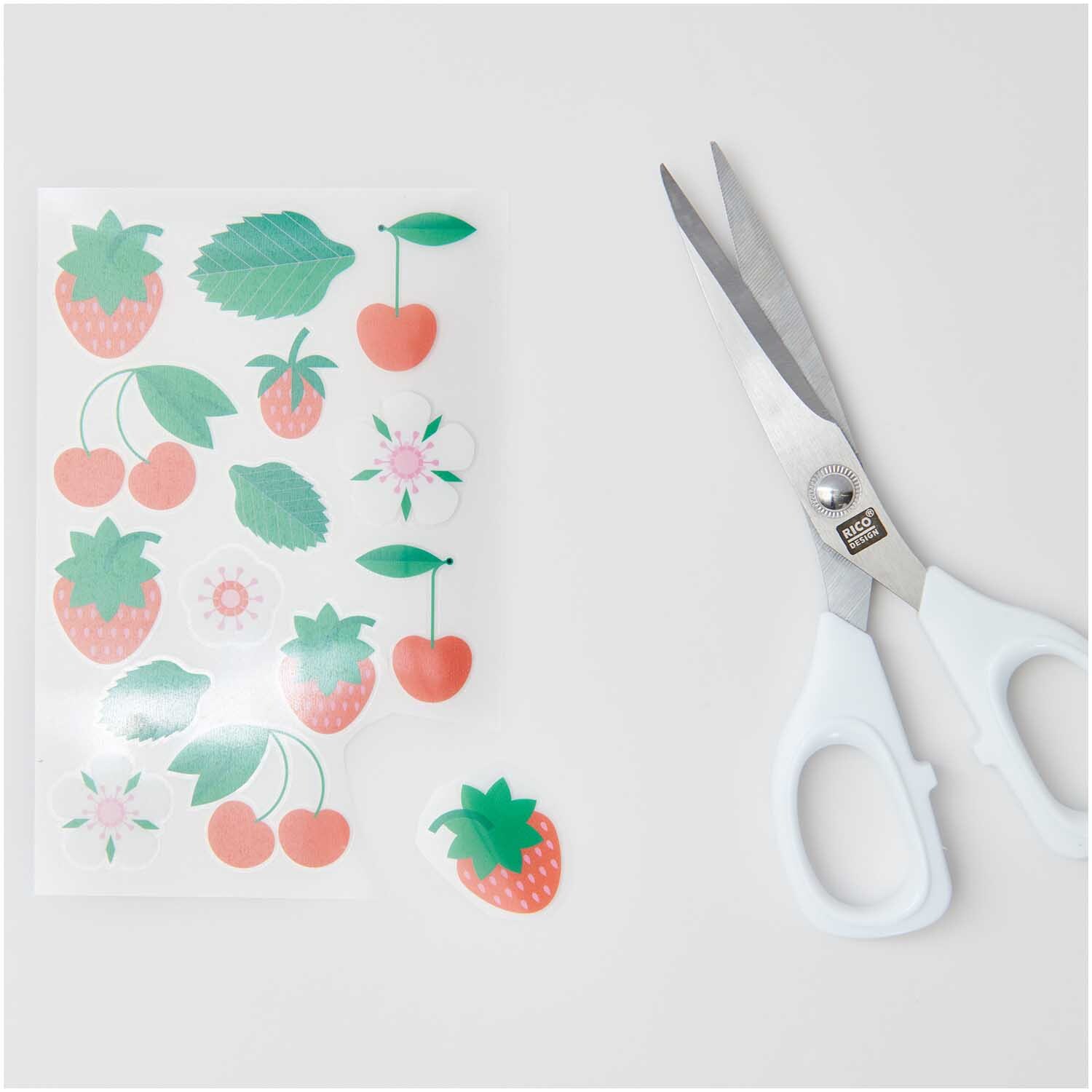 Transfermotiv Früchte & Blumen: Bogen mit bunten Frucht- und Blumenmotiven von Rico Design neben einer Schere.