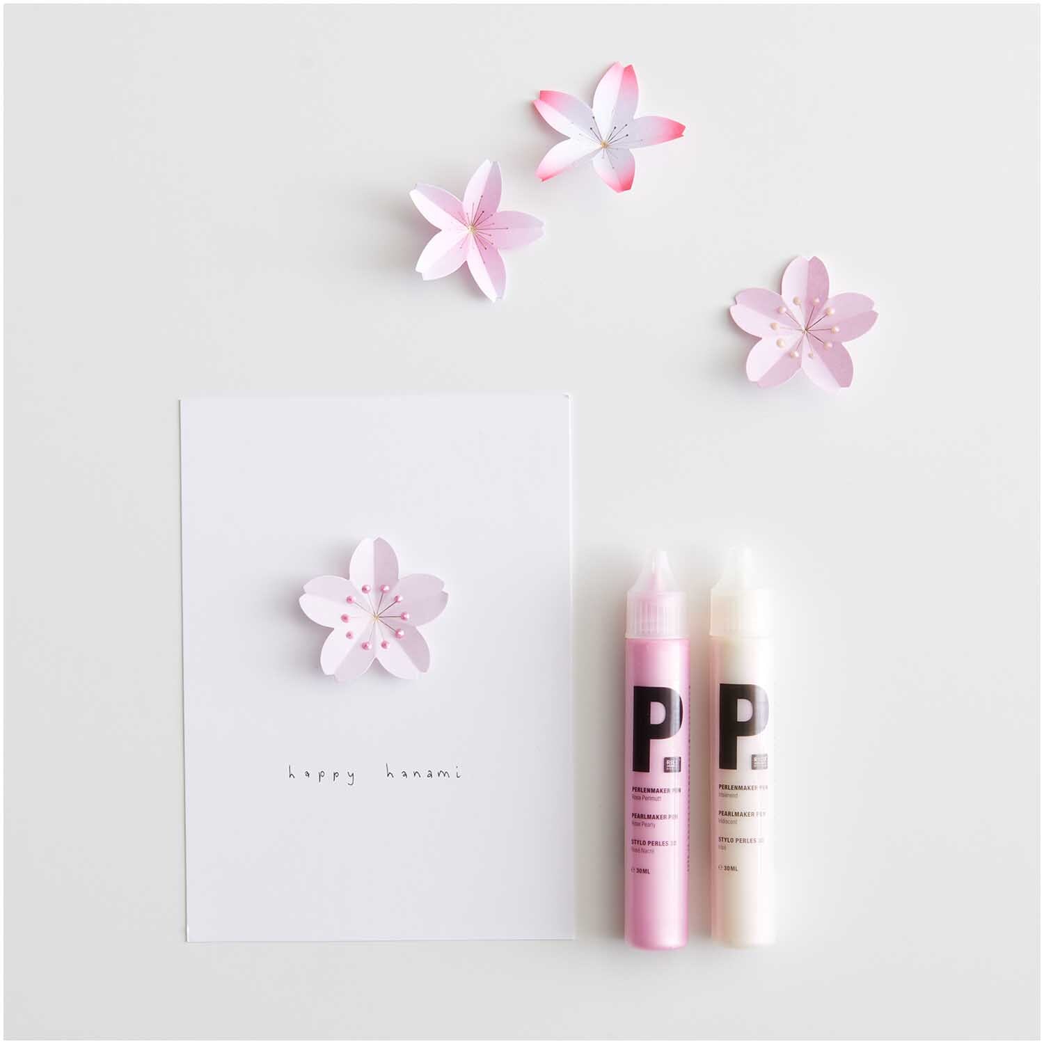 Paper Poetry Mini-Papierblüten Luxury Sakura in Rosa, arrangiert mit zwei Bastelstiften und einer Karte auf weißem Hintergrund.