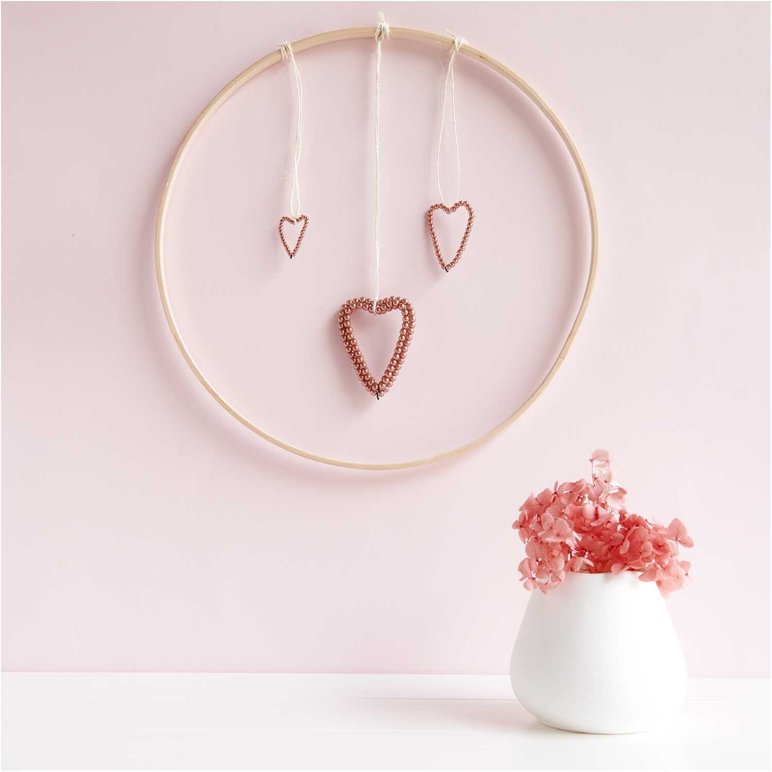 Pendentif perles coeur petit or rose from Rico Design Perlenhänger Herz klein rosegold: Drei herzförmige Anhänger aus Perlen an einem Ring vor rosa Hintergrund.