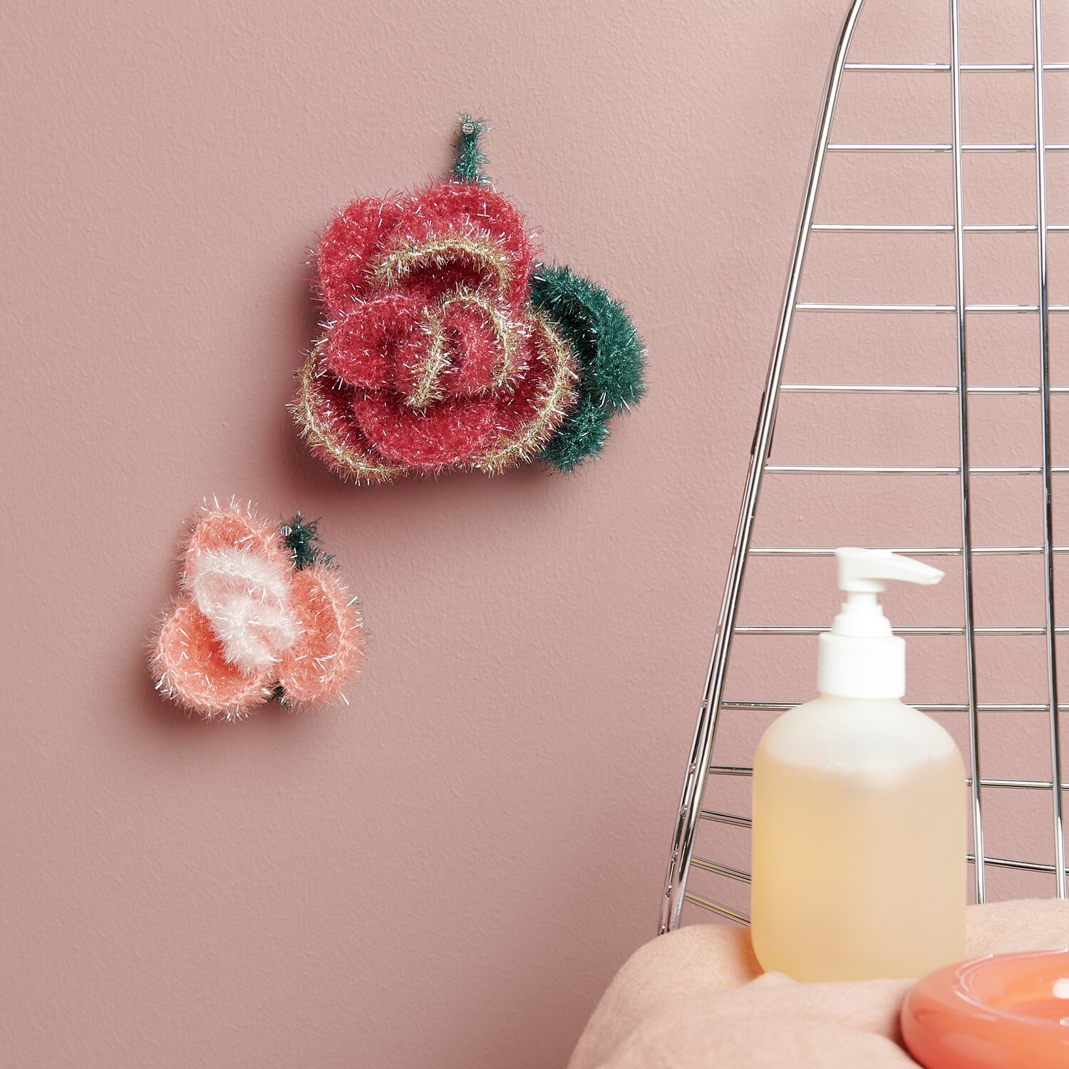 Häkelset Creative Bubble Rose Romantic von Rico Design Häkelset Creative Bubble Rose Romantic: Zwei gehäkelte Rosen in Rosa und Grün an einer rosa Wand.
