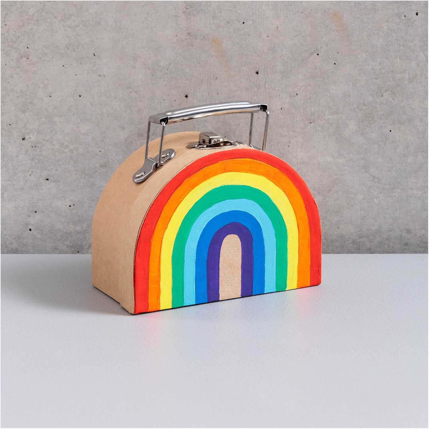 Koffer aus Pappe halbrund natur von Rico Design mit Regenbogenmotiv auf grauem Hintergrund.