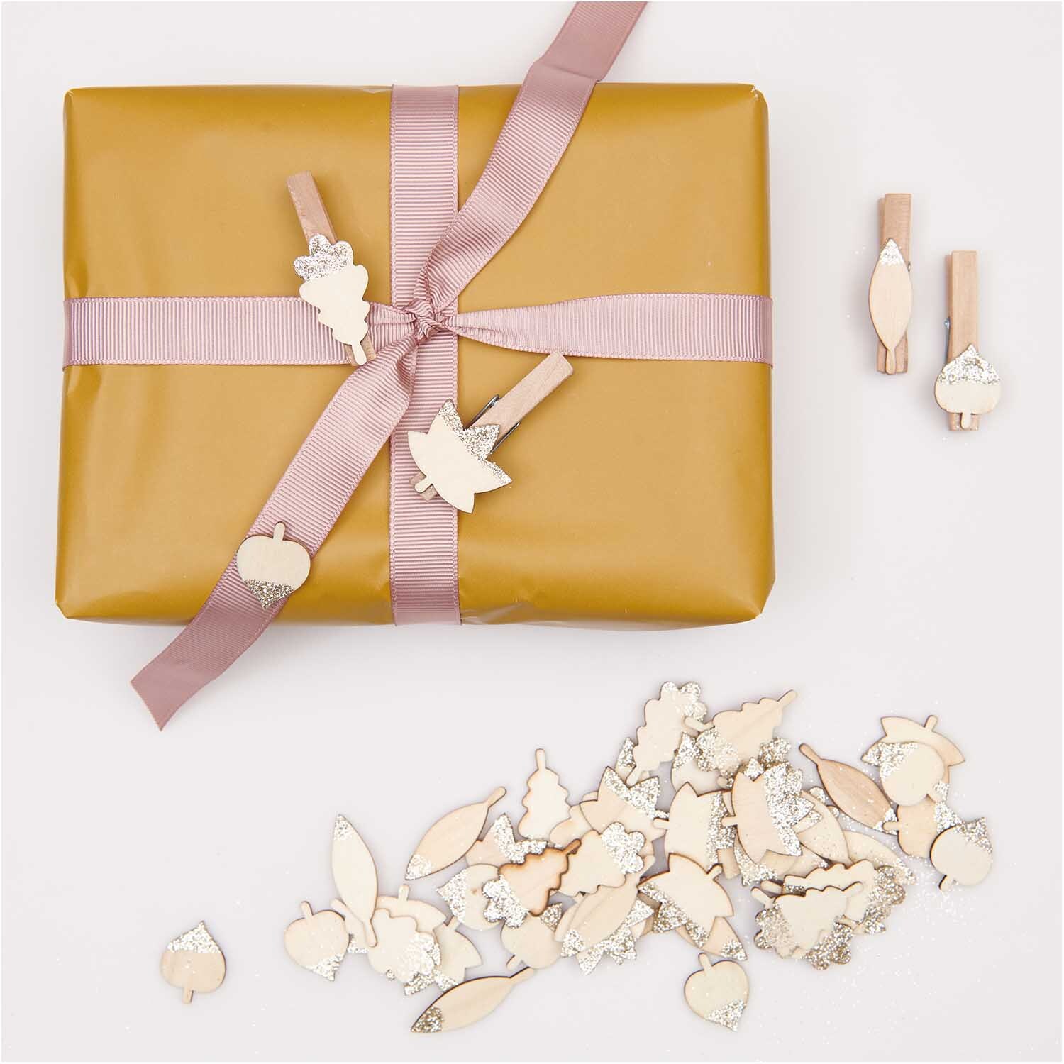 Holzstreu Blätter Mix mit Glitter natur-gold 48 Stück von Rico Design Holzstreu Blätter Mix mit Glitter natur-gold 48 Stück, dekorativ auf Geschenk mit rosa Band arrangiert.