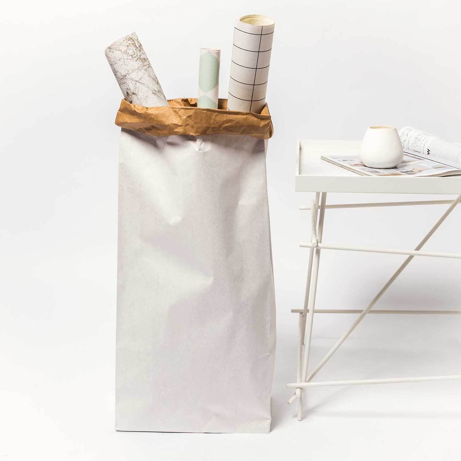 Paper Poetry Maxi-Blockbodenbeutel XL 76x32x18cm 1 Stück Farbe Weiß-Braun von Rico Design Paper Poetry Maxi-Blockbodenbeutel XL, weiß-braun, neben einem Tisch, gefüllt mit Papierrollen.