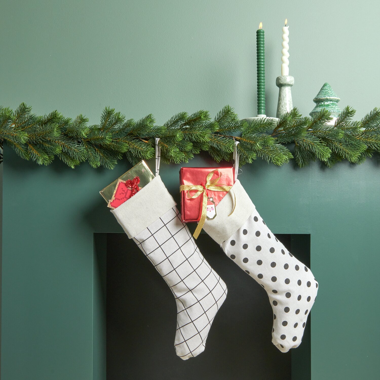 Weihnachtssocke gepunktet Weiß-Schwarz 45x22cm von Rico Design Weihnachtssocke gestreift und gepunktet hängen an einem Kamin, dekoriert mit Tannenzweigen und Kerzen.