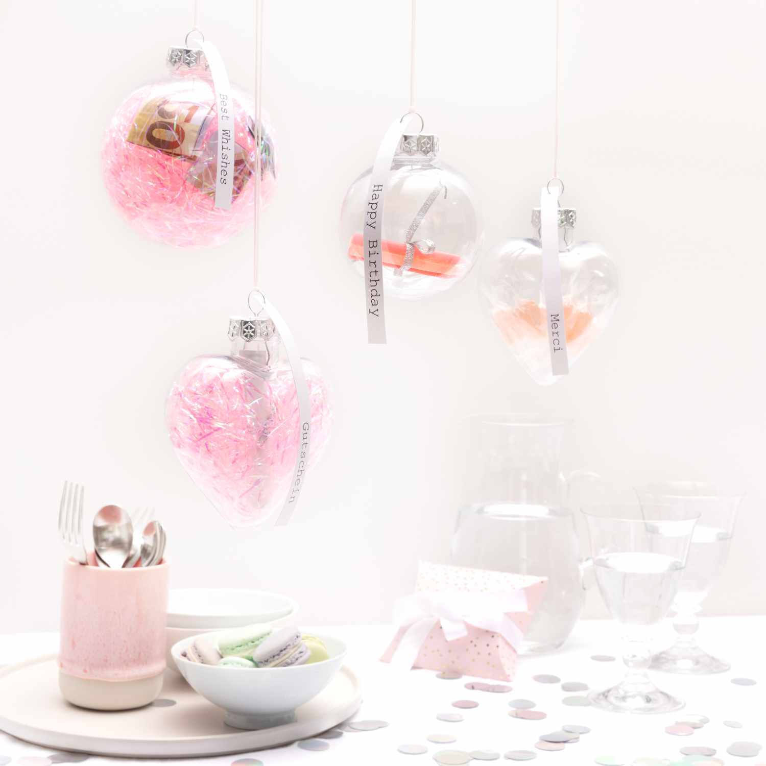 Weihnachtskugel aus Kunststoff 7cm von Rico Design Weihnachtskugel aus Kunststoff 7cm, dekoriert mit rosa Füllung, hängt neben Besteck und Gläsern.