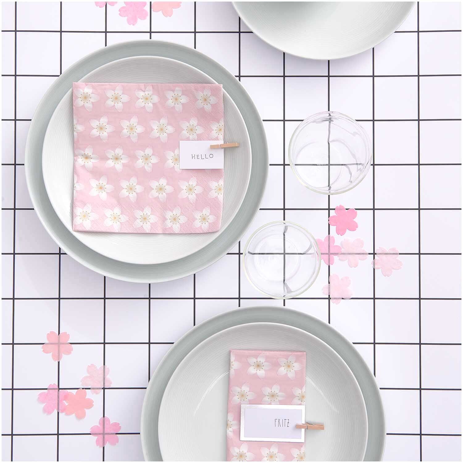 Konfetti Kirschblüten pastell rosa Mix 20g von Rico Design auf einem gedeckten Tisch mit rosa Blütenmuster-Servietten und transparenten Gläsern.