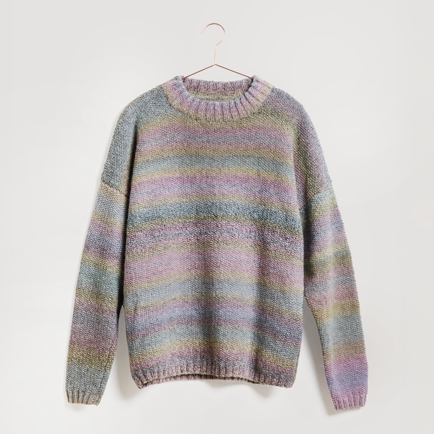 Creative Melange Alpaca Wonderball dk 100g 300m Farbe Pastels von Rico Design Ein gestrickter Pullover in sanften Pastelltönen hängt an einem Kleiderbügel. Der Pullover zeigt ein Streifenmuster in Blau, Rosa und Grün. Marke: Modell Legeware. Perfekt für einen gemütlichen Look.