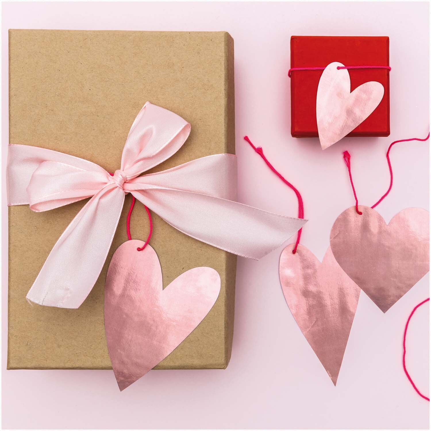 Paper Poetry Papieranhänger in Herzform, dekorativ an Geschenkboxen mit rosa Schleife befestigt. Ideal für romantische Anlässe.