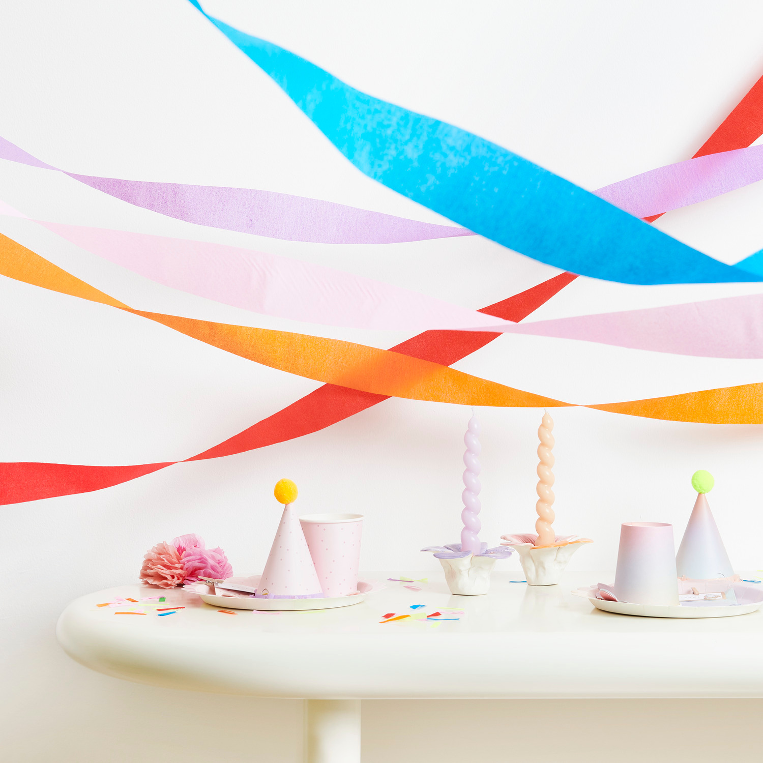 Kreppbänder extra breit Regenbogen Klassik Mix 5,5cmx10m 9 Stück von Rico Design Kreppbänder extra breit Regenbogen Klassik Mix dekorieren einen Tisch mit Partyhüten und Kerzen.