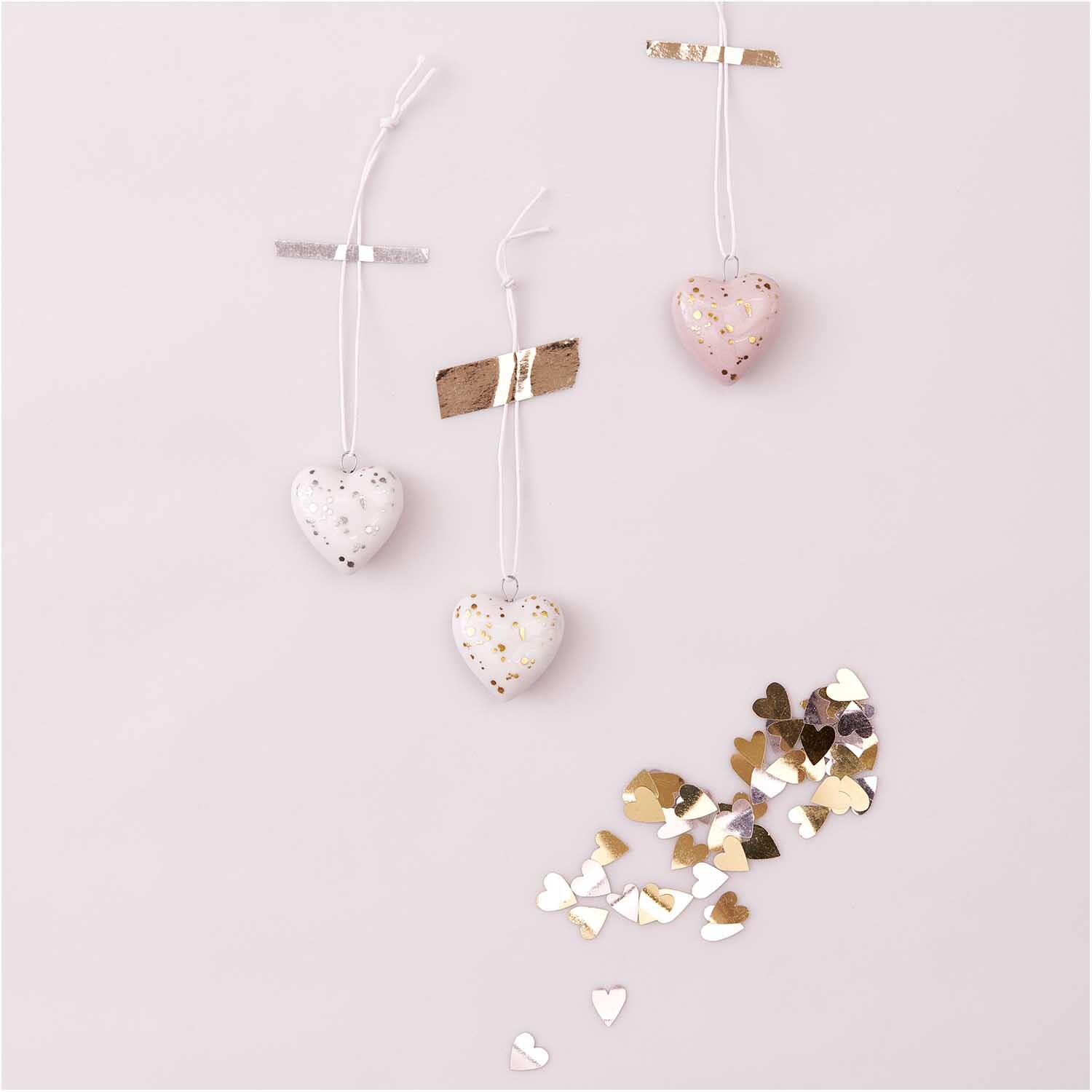 Porzellanhänger Herz rosa-gold 35x35mm von Rico Design Porzellanhänger Herz rosa-gold: Drei herzförmige Anhänger in Rosa und Weiß mit goldenen Akzenten, dekorativ aufgehängt.