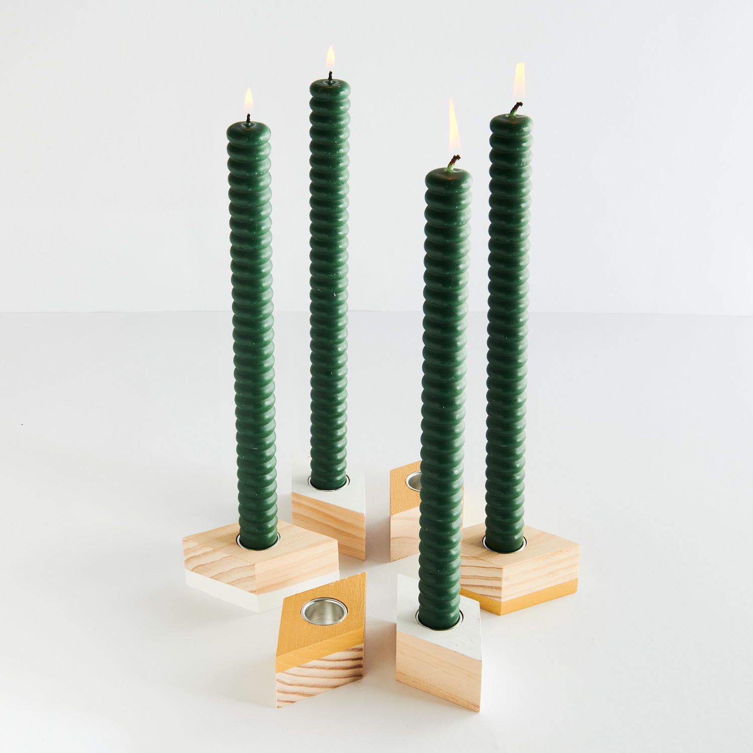 Kerzenhalter Raute für Stabkerzen von Rico Design, aus Holz, präsentiert mit vier grünen Kerzen.