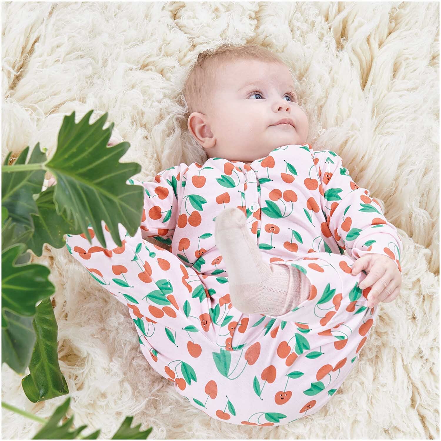 Stoffabschnitt Jersey bedruckt Kirschen rosa 80x100cm von Rico Design Stoffabschnitt Jersey bedruckt Kirschen rosa 80x100cm: Baby in Kirschmuster-Outfit auf weichem, cremefarbenem Teppich liegend.