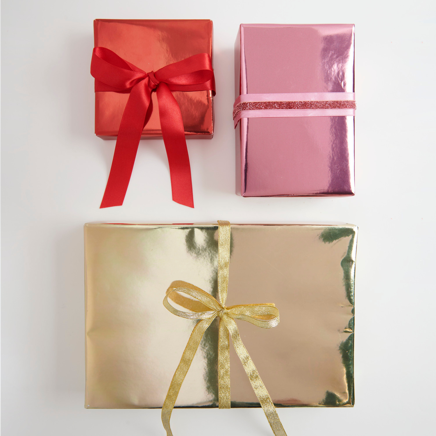 Metallic Band Gold Glitzer Breite 13mm von Rico Design Geschenkpapier Metallic: Drei glänzende Geschenke in Gold, Rot und Pink mit Satinband verziert.