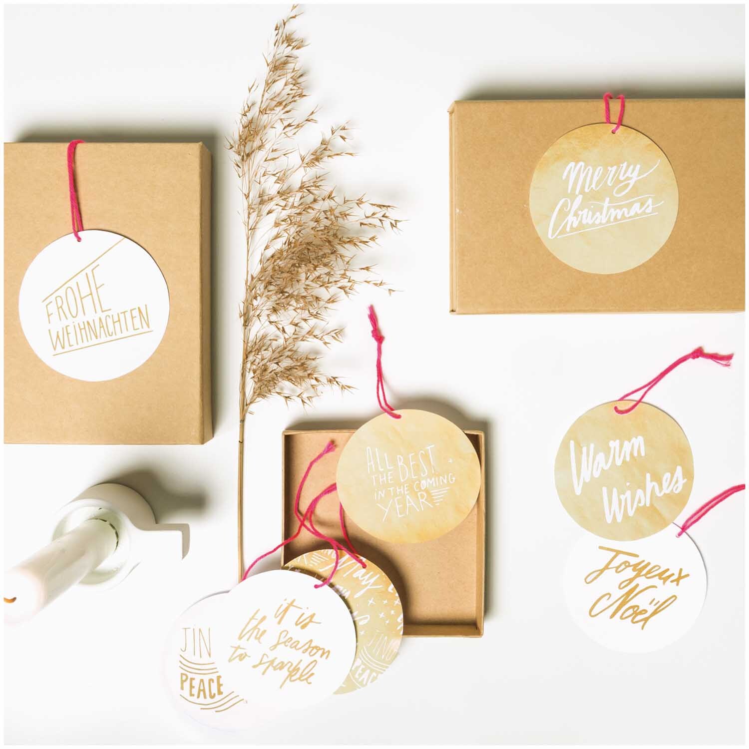 Paper Poetry Papieranhänger Jolly Christmas: Runde Anhänger mit festlichen Botschaften in Gold auf braunen Boxen arrangiert. Ideal für Weihnachtsgeschenke.