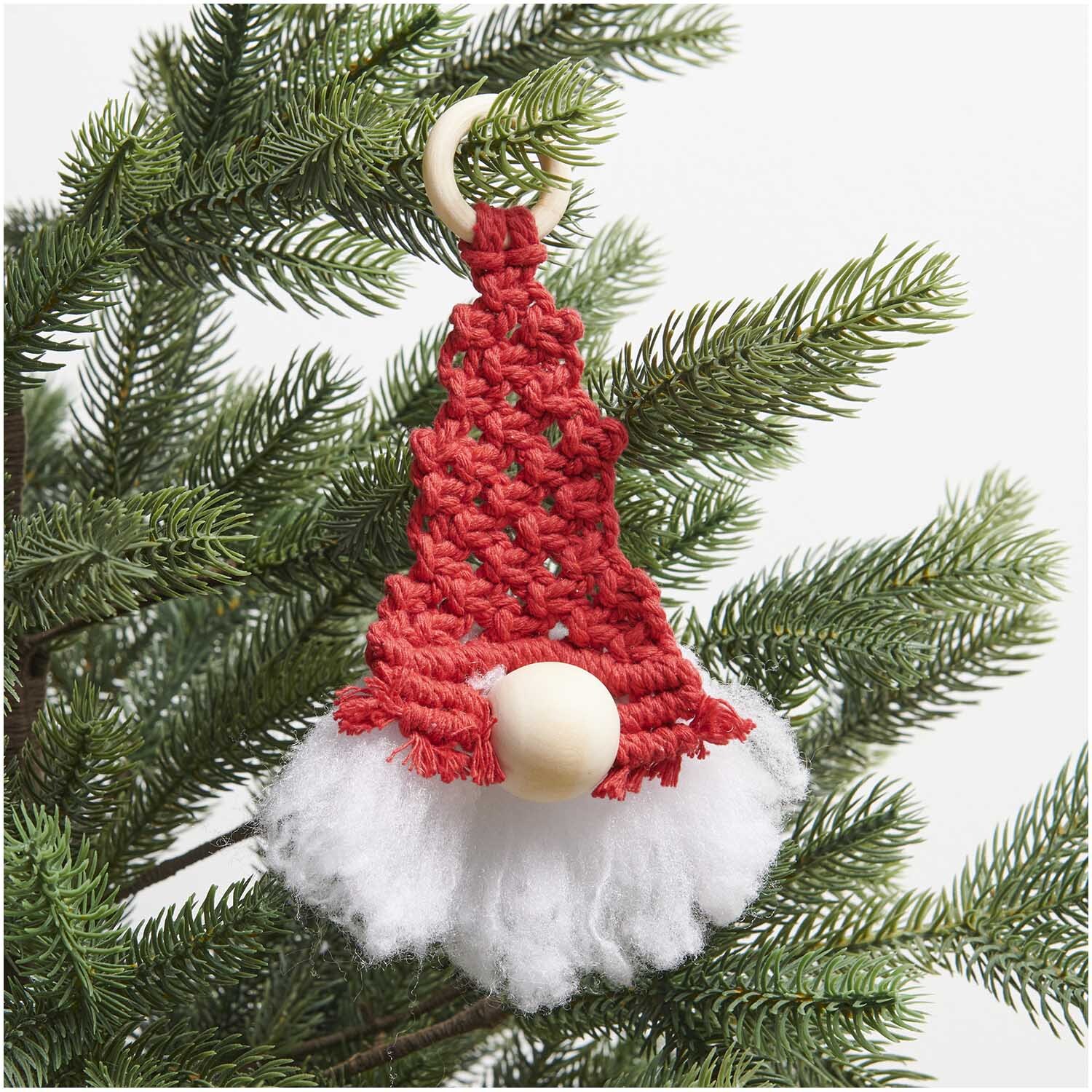 Set macramé lutin 20x8cm from Rico Design Makramee Set Wichtel 20x8cm von Rico Design: Roter Wichtel aus Makramee mit weißem Bart, hängend an einem Tannenzweig.