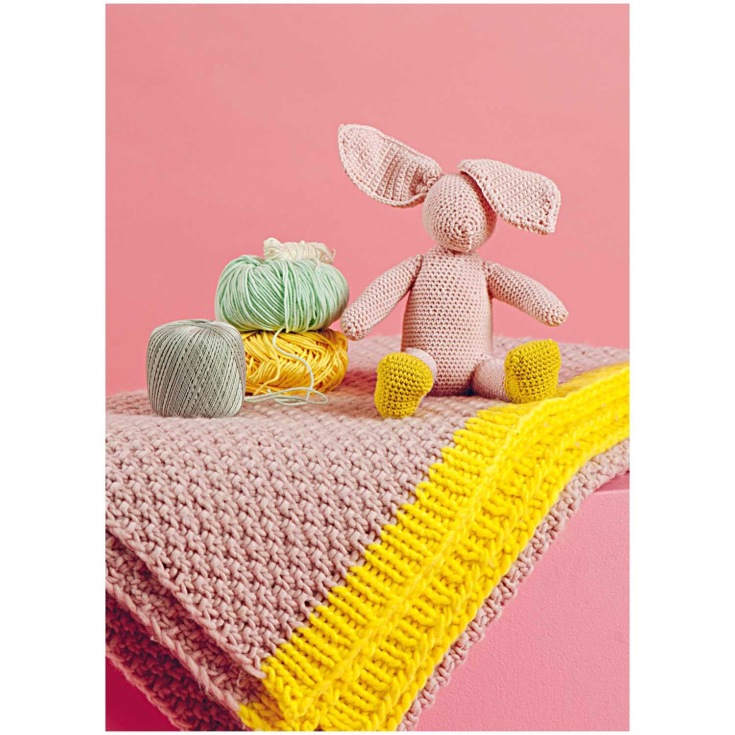 Füllwatte: Ein gehäkelter Hase sitzt auf einer rosa Decke mit gelbem Streifen, umgeben von Garnknäueln. Marke: Rico Design.