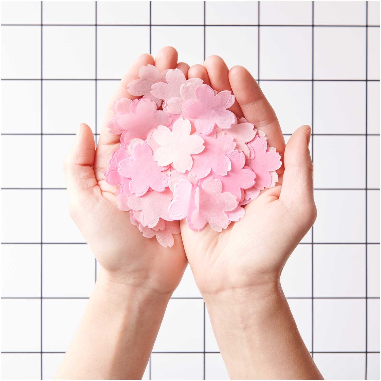 Konfetti Kirschblüten pastell rosa Mix 20g von Rico Design in Händen vor kariertem Hintergrund.