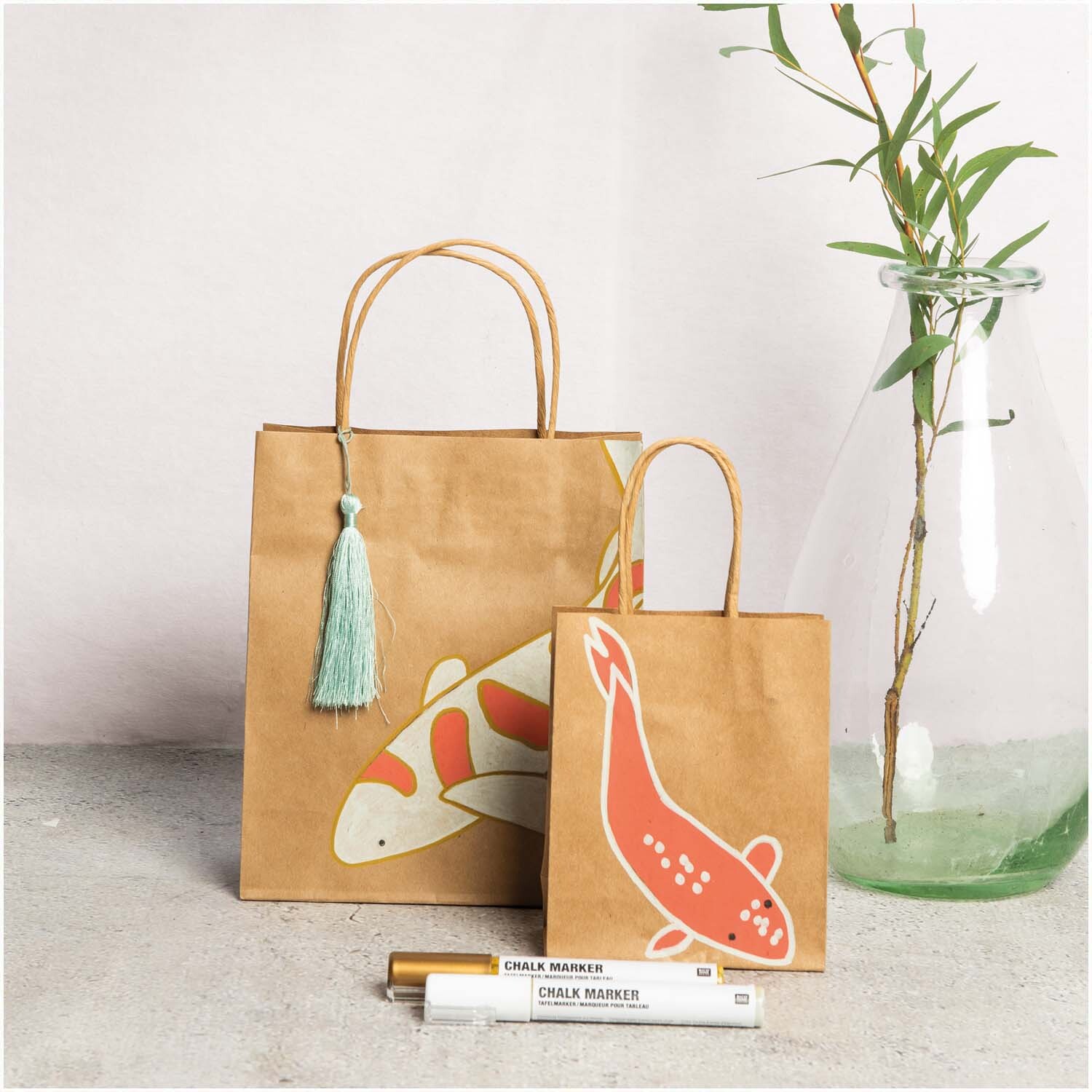 Kreidestifte Flüssigkreide Set Natur 3mm 6 Farben von Rico Design Kreidestifte Flüssigkreide Set Natur 3mm 6 Farben von Rico Design vor zwei Papiertüten mit Koi-Motiven und einer Vase mit Bambus.