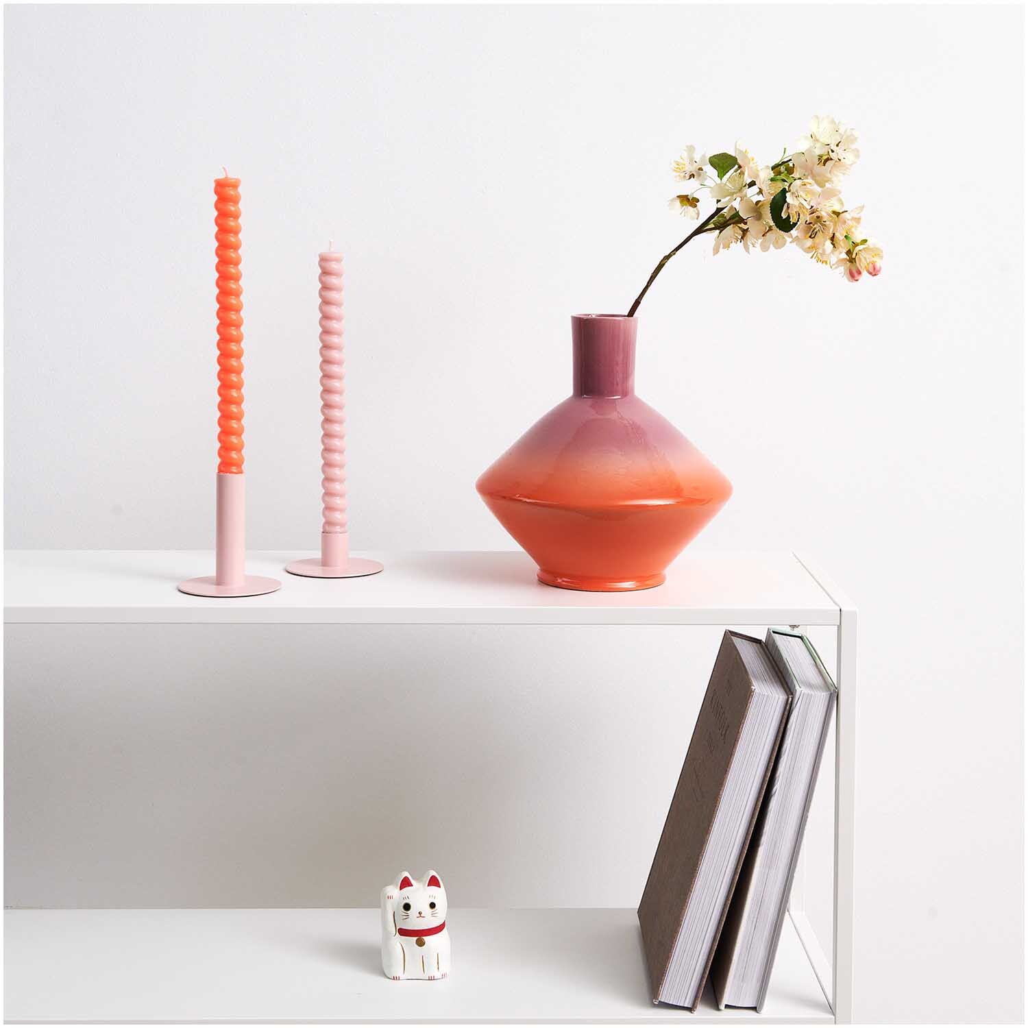 Spiralkerze 2,4x28cm in Neon Orange von Rico Design neben einer Vase mit Blumen auf einem Regal.