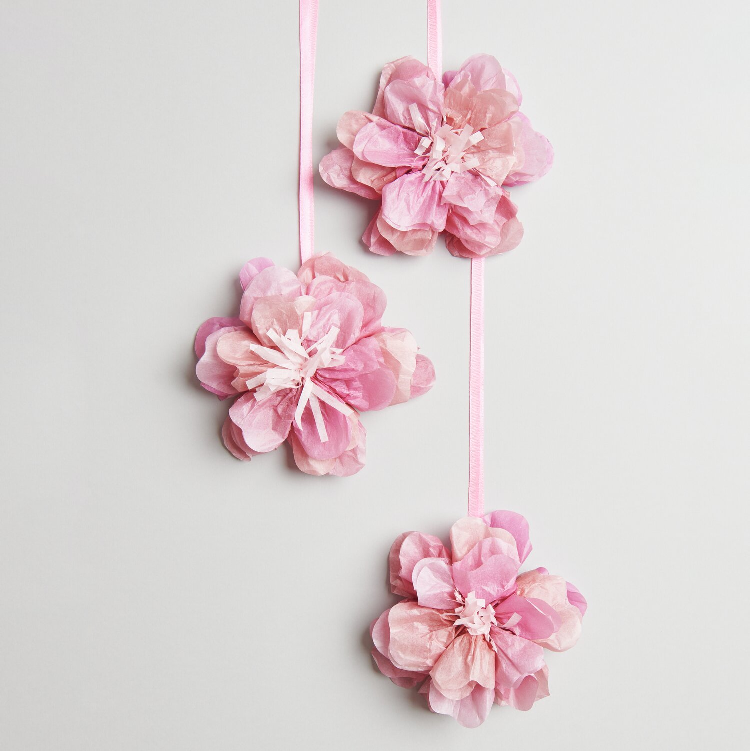 Seidenpapierblumen Wildrose Rosa: Drei zarte, rosa Papierblumen von Rico Design, dekorativ an Bändern hängend.