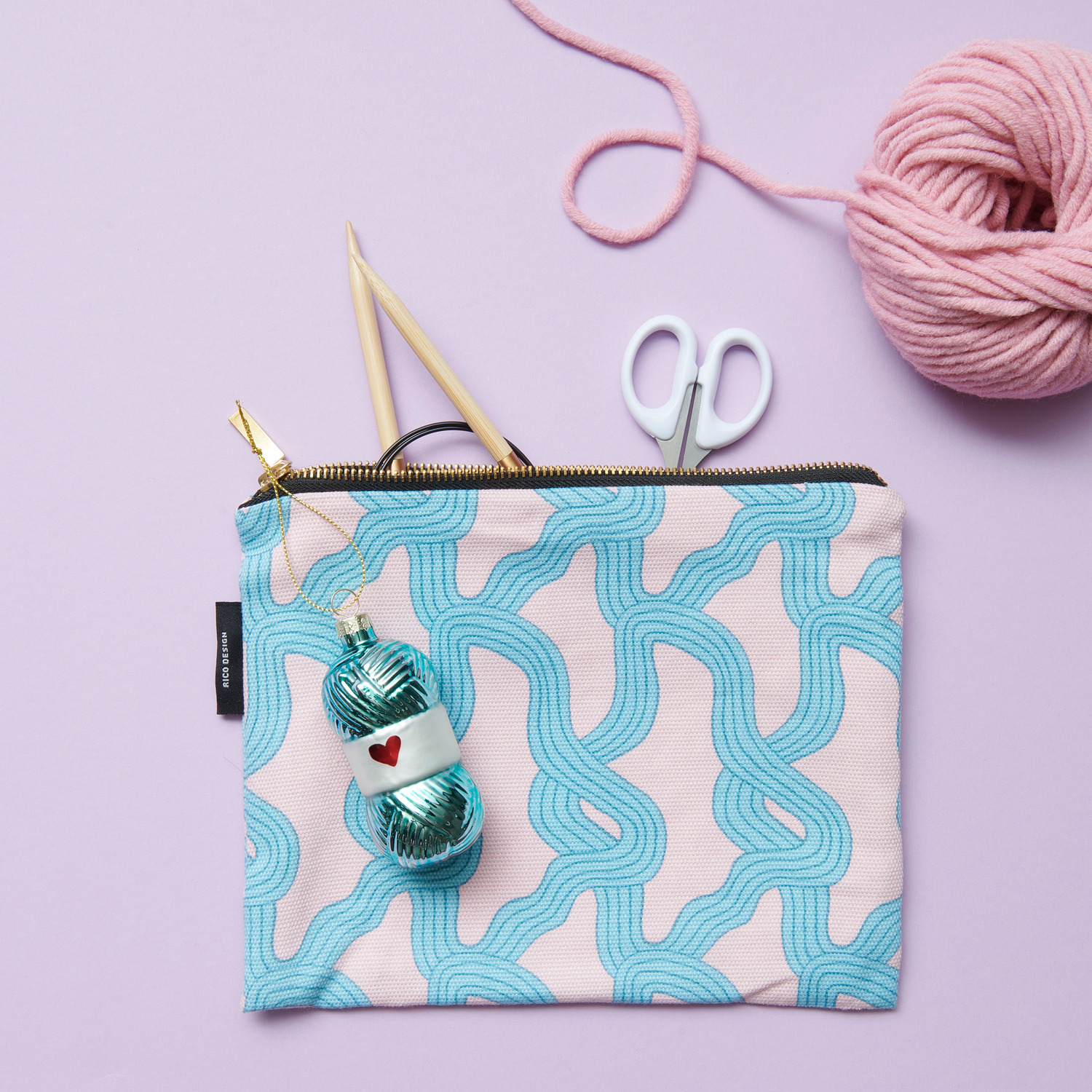 Canvas-Pouches Myzel Rosa 17x23cm von Rico Design Canvas-Pouches Myzel Rosa mit blauem Muster, gefüllt mit Stricknadeln, Schere und Garn auf lila Hintergrund. Größe: 17x23cm.