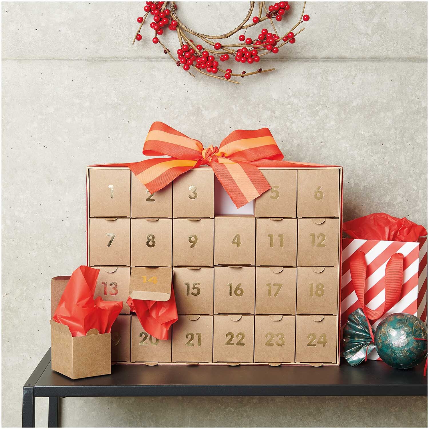 Adventskalender zum Befüllen 36,5x29x6cm Farbe Kraftpapier-Gold von Rico Design Adventskalender zum Befüllen aus Kraftpapier-Gold mit roten Schleifen, dekoriert auf einem Tisch.