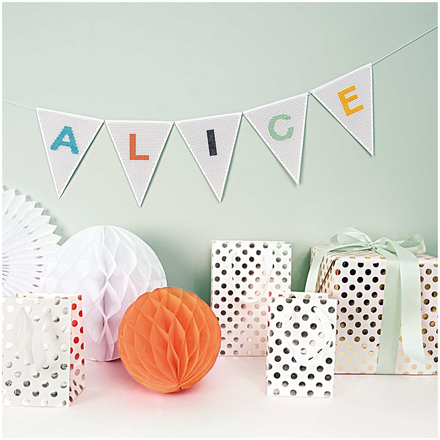 Geschenktüte weiß Punkte silber 12x18x10cm von Rico Design Geschenktüte weiß Punkte silber 12x18x10cm vor einer Dekoration mit Wimpelkette und Geschenkboxen.