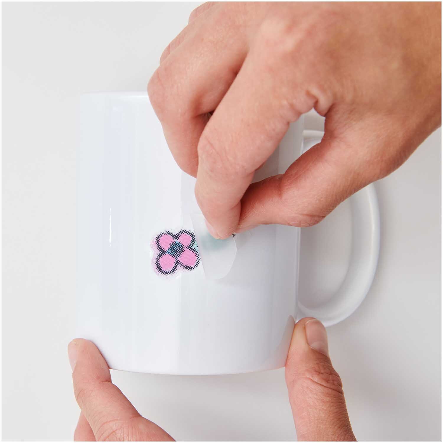 Transfermotiv Spray-Mix 10 Stück von Rico Design Transfermotiv Spray-Mix 10 Stück: Hände kleben ein buntes Blumenmotiv auf eine weiße Tasse. Marke: Rico Design.