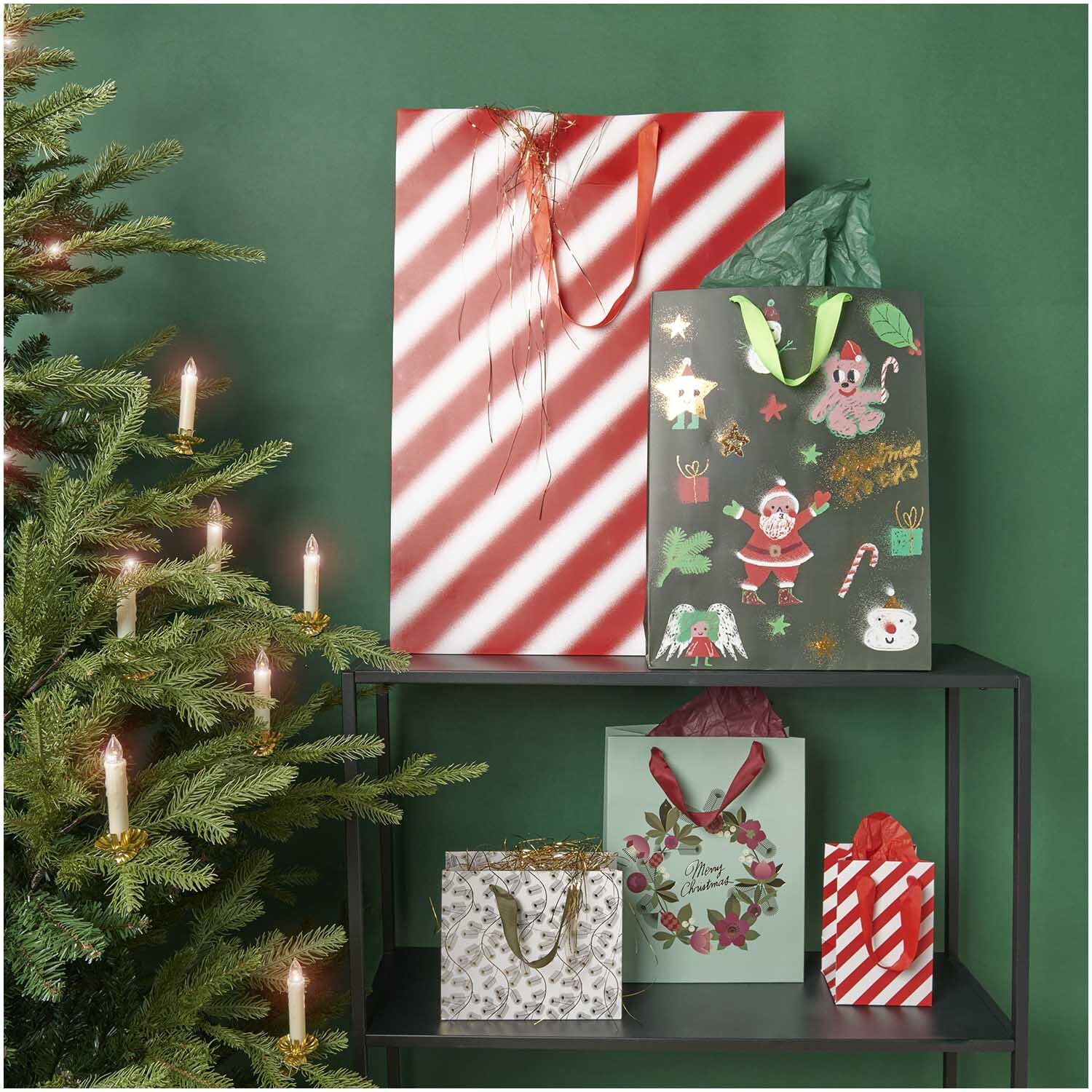 Paper Poetry Geschenktüte Streifen rot-weiß 12x18x10cm von Rico Design Paper Poetry Geschenktüte mit rot-weißen Streifen, dekorativ neben einem Weihnachtsbaum platziert.