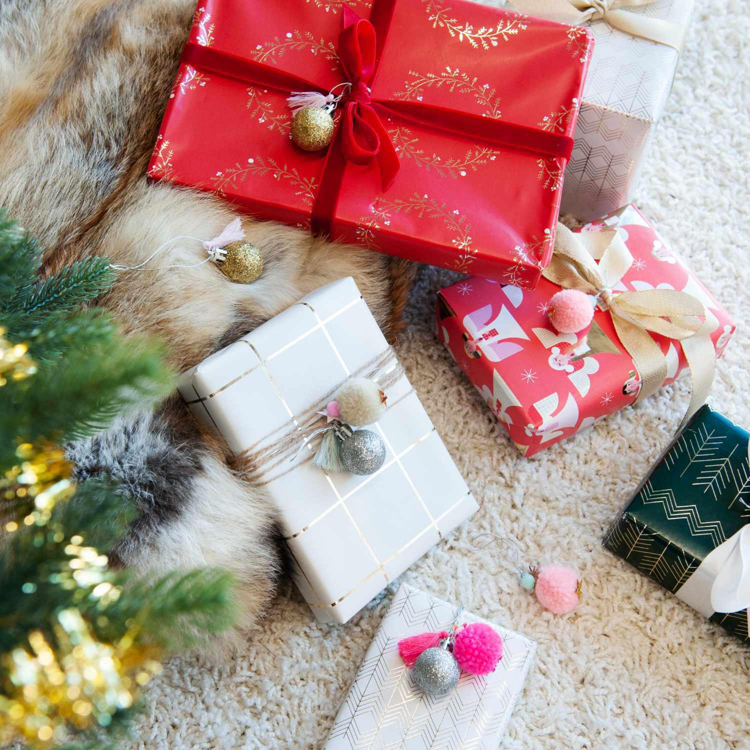 Pompon- und Kugel-Anhänger gold-silber 6 Stück von Rico Design schmücken festlich verpackte Geschenke auf einem Teppich neben einem Weihnachtsbaum.