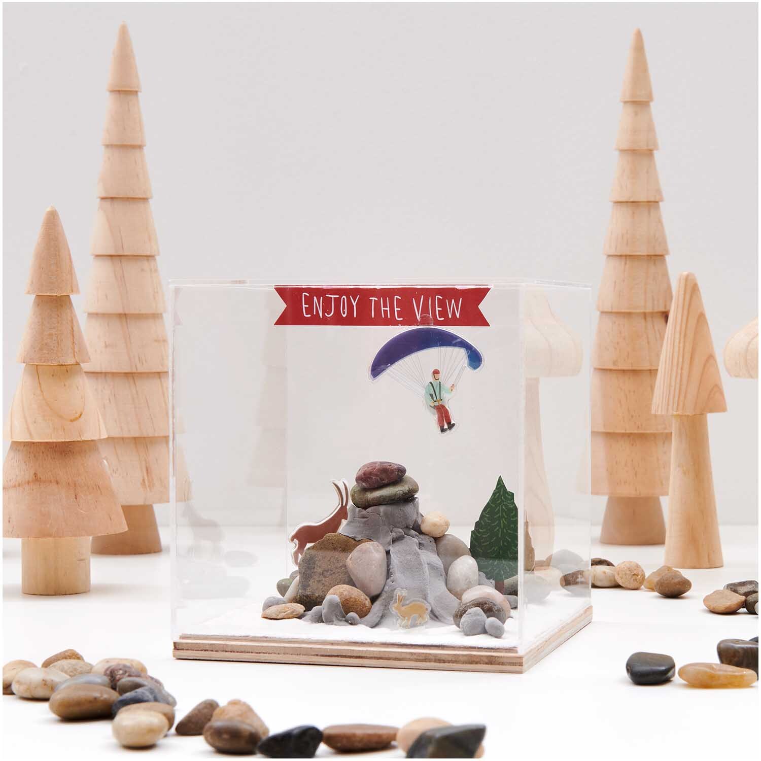 Figurico Modelliermasse 28g Farbe Grau von Rico Design Figurico Modelliermasse 28g: Diorama mit Holzfiguren, Steinen und einem Paraglider in einer klaren Box.