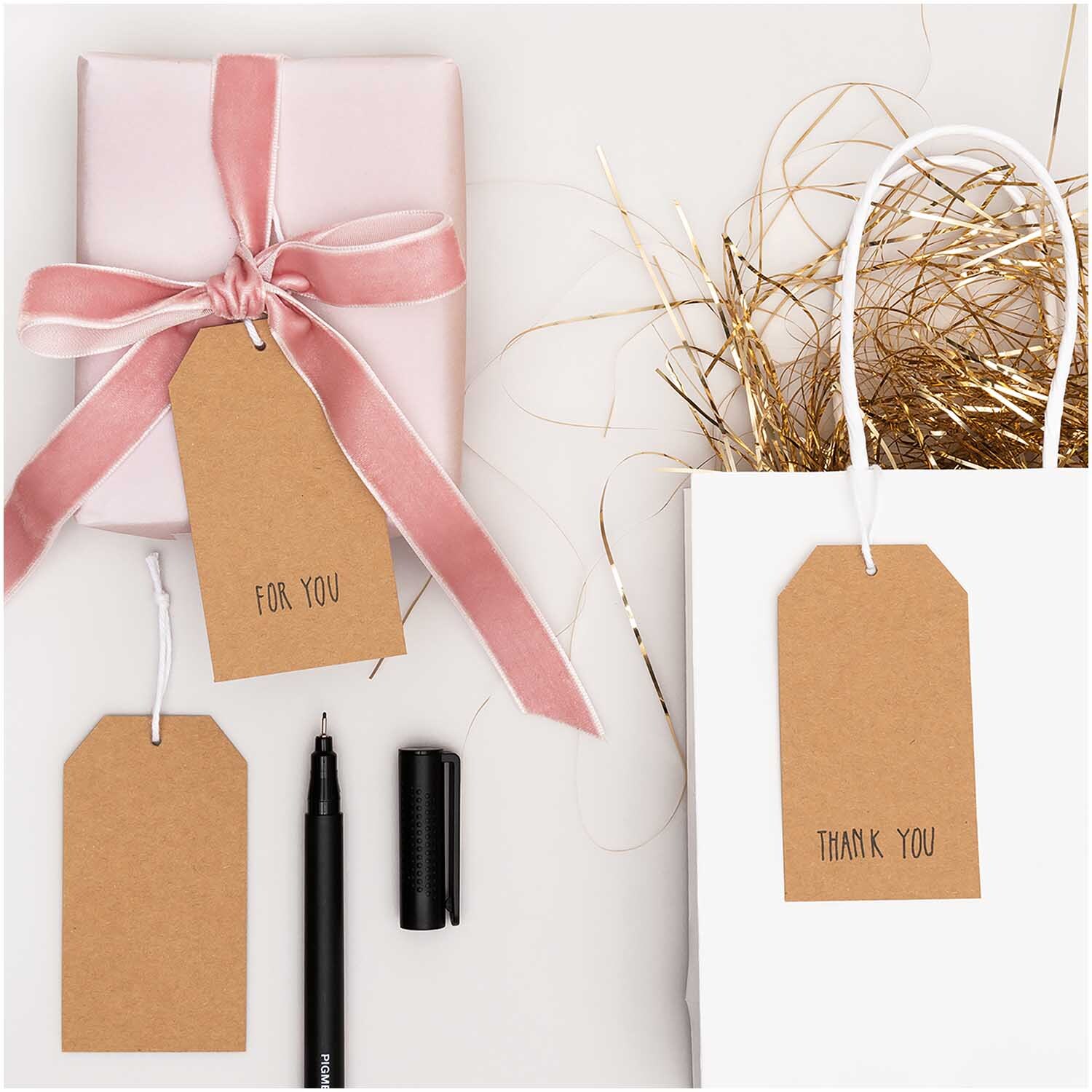 Paper Poetry Papieranhänger Kraftpapier 24 Stück Größe 4,5x8cm von Rico Design Paper Poetry Papieranhänger Kraftpapier 24 Stück, dekoriert mit rosa Geschenkband und weißer Geschenktüte, ideal für kreative Verpackungen.
